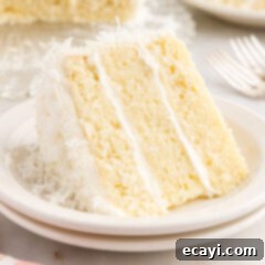 Tropical Cloud Cake 6 Slice of Coconut Cake with cream cheese frosting and shredded coconut on a white plate