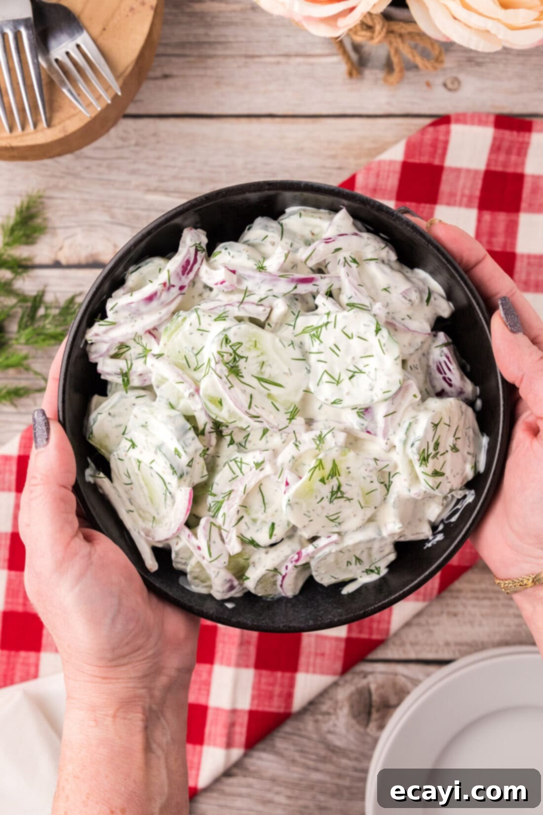 Cool and Creamy Cucumbers 2 Hands holding a bowl of Creamy Cucumber Salad, garnished with fresh dill.