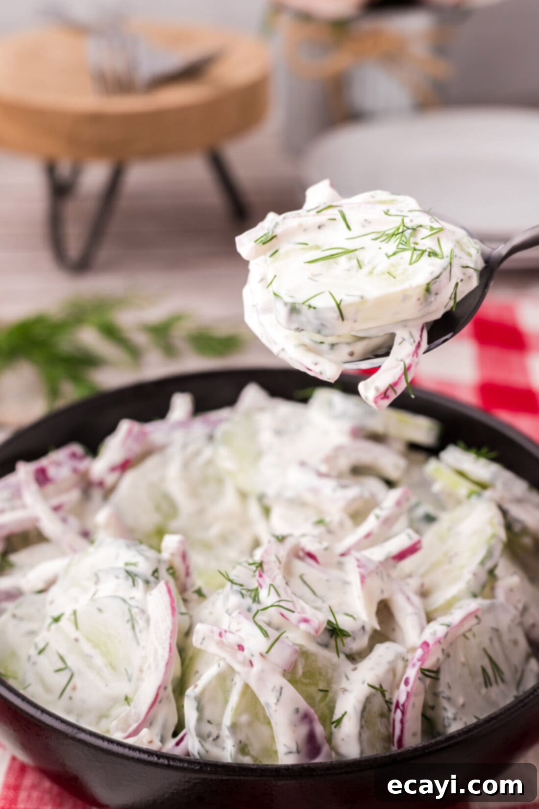 Cool and Creamy Cucumbers 6 A spoonful of Creamy Cucumber Salad held gracefully above a full bowl, highlighting its creamy texture and fresh ingredients.