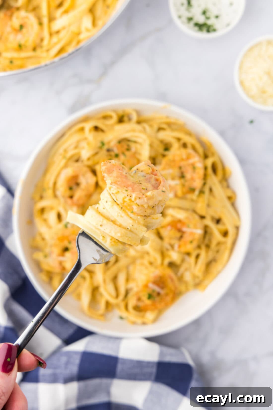Shrimp Alfredo Bliss 14 Shrimp Alfredo twisted around a fork held above a bowl of Shrimp Alfredo, highlighting the creamy sauce and tender pasta