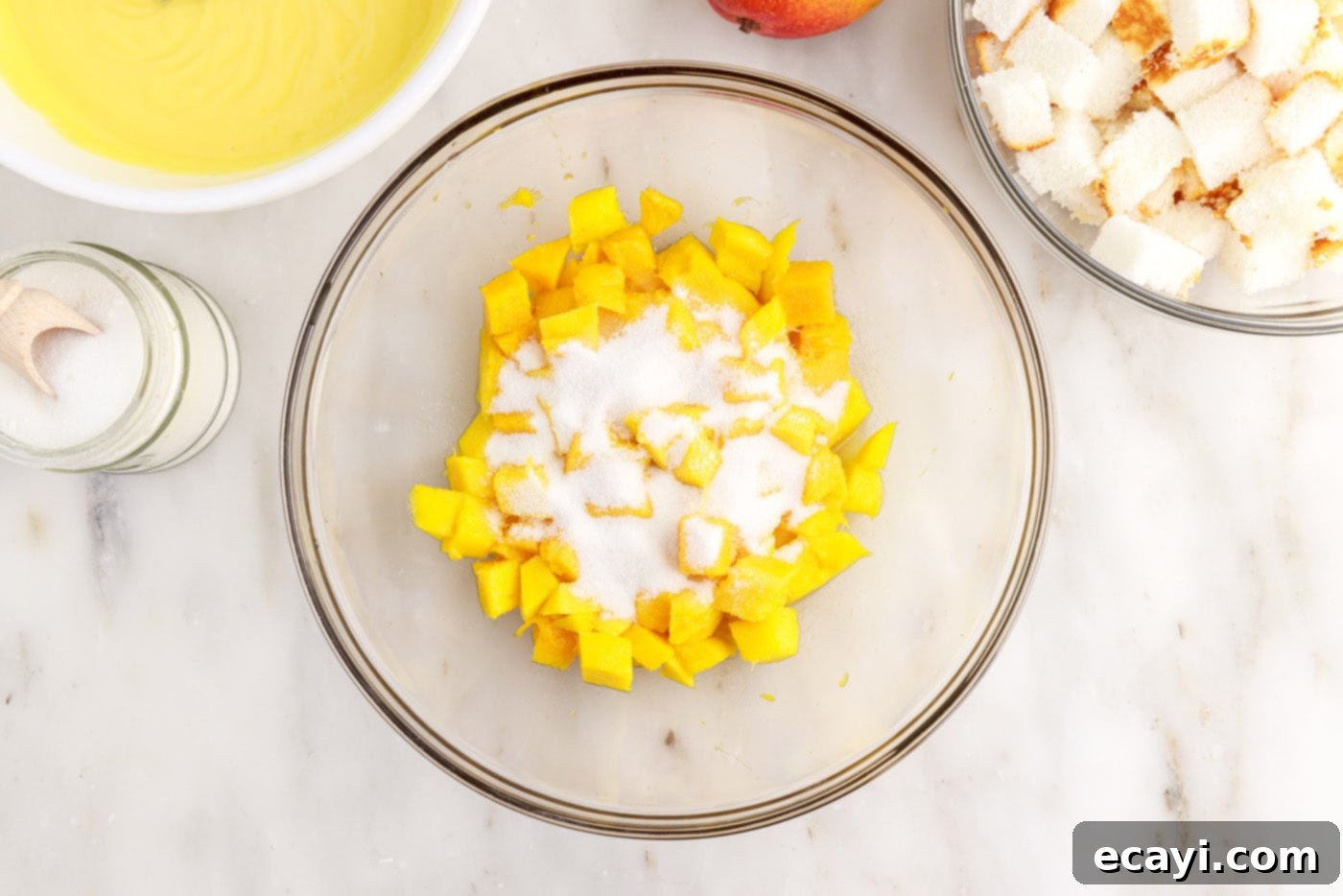 Golden Mango Indulgence 7 Granulated sugar being sprinkled over freshly diced mangoes in a bowl.