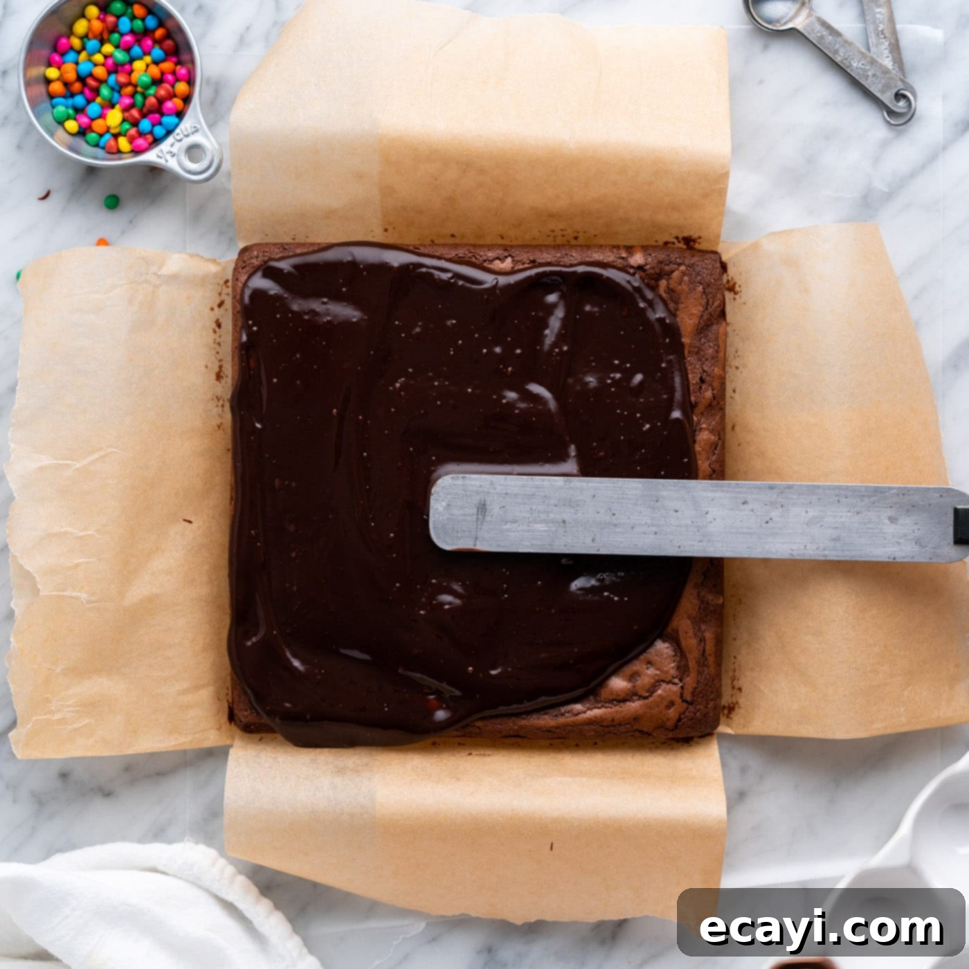 Dark Matter Delights 19 Spreading a layer of rich chocolate ganache over cooled brownies in a pan.