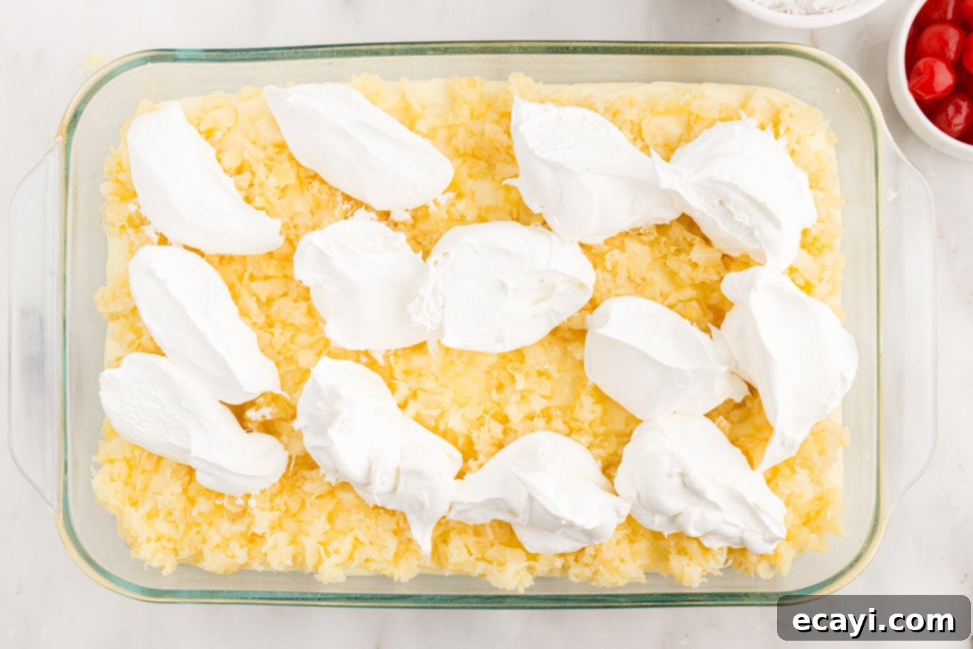 Billionaire Bliss Cake 12 Dollops of Cool Whip being spread over the crushed pineapple layer on the Millionaire's Cake.