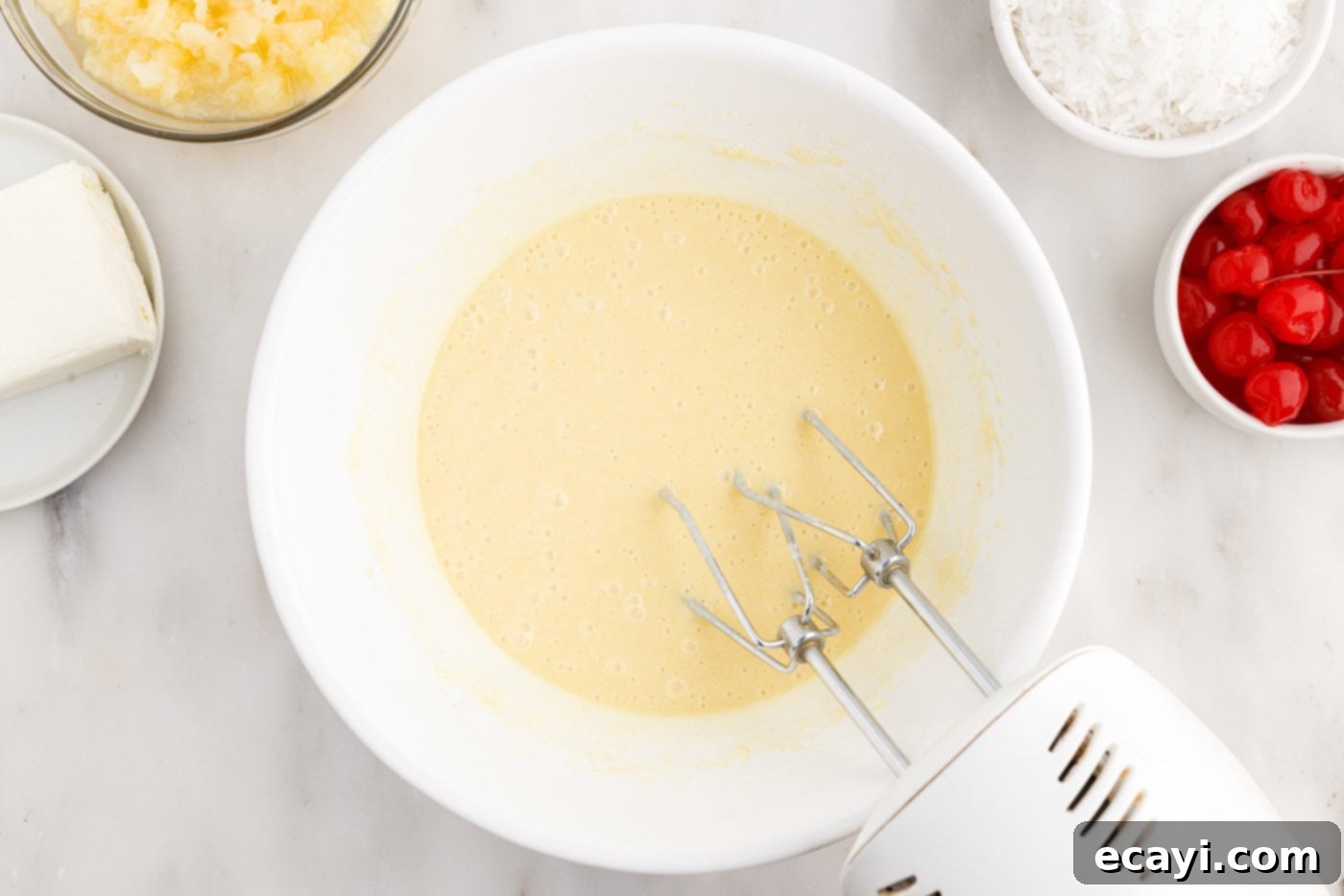 Billionaire Bliss Cake 6 Cake mix being blended in a bowl with a hand mixer, achieving a smooth batter consistency.