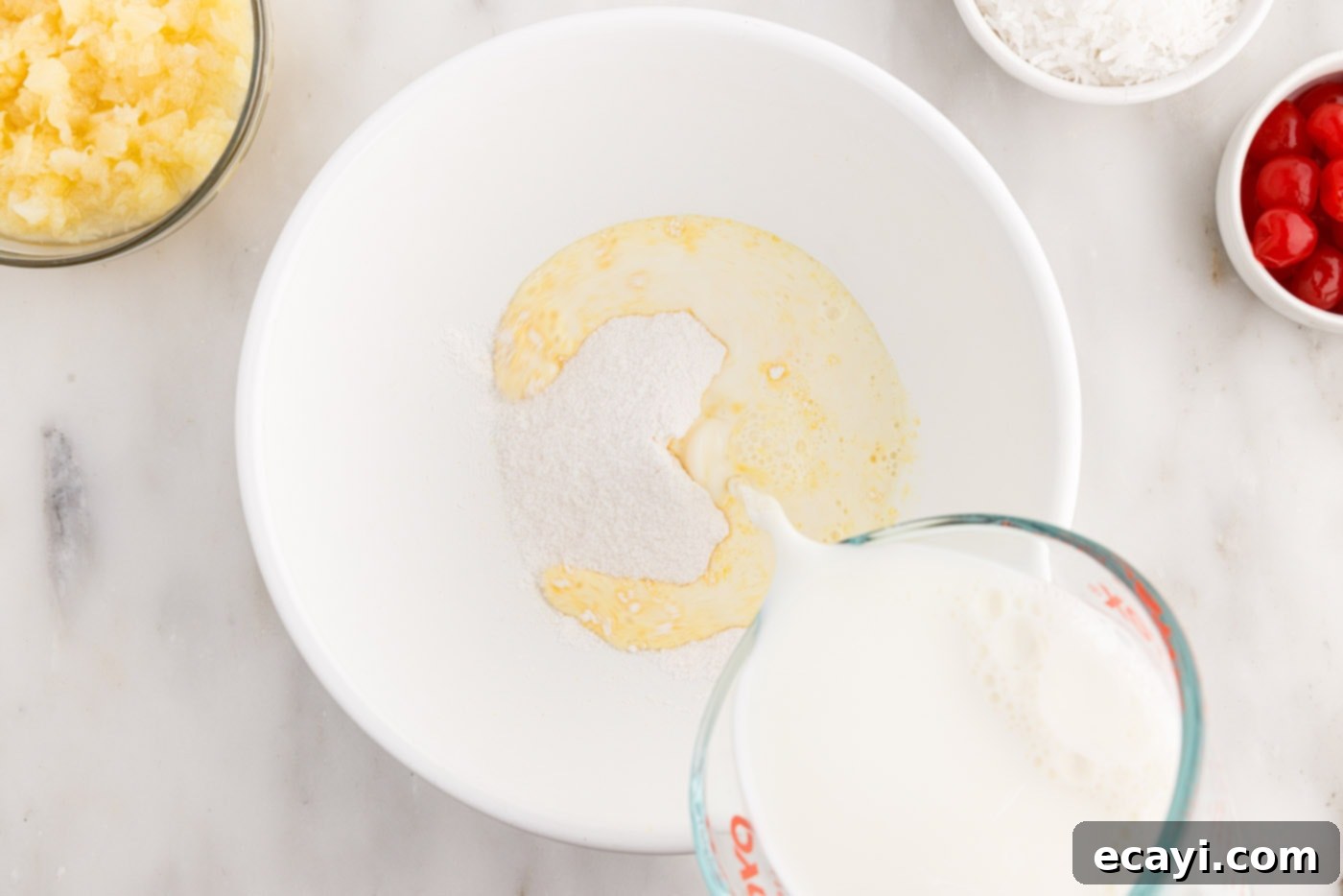 Billionaire Bliss Cake 8 Pouring milk into vanilla pudding mix in a bowl, beginning the pudding layer for Millionaire's Cake.