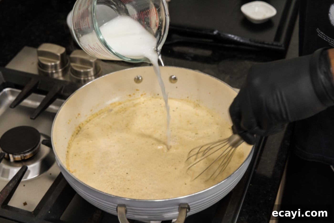 Creamy Cajun Shrimp Pasta 13 Pouring the cornstarch slurry into the simmering cream sauce in the skillet to thicken it, with a whisk nearby.