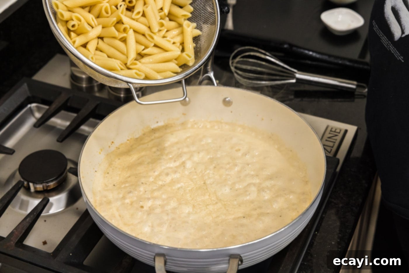 Creamy Cajun Shrimp Pasta 14 Adding al dente penne pasta to the creamy Cajun sauce in the skillet, ready for stirring.