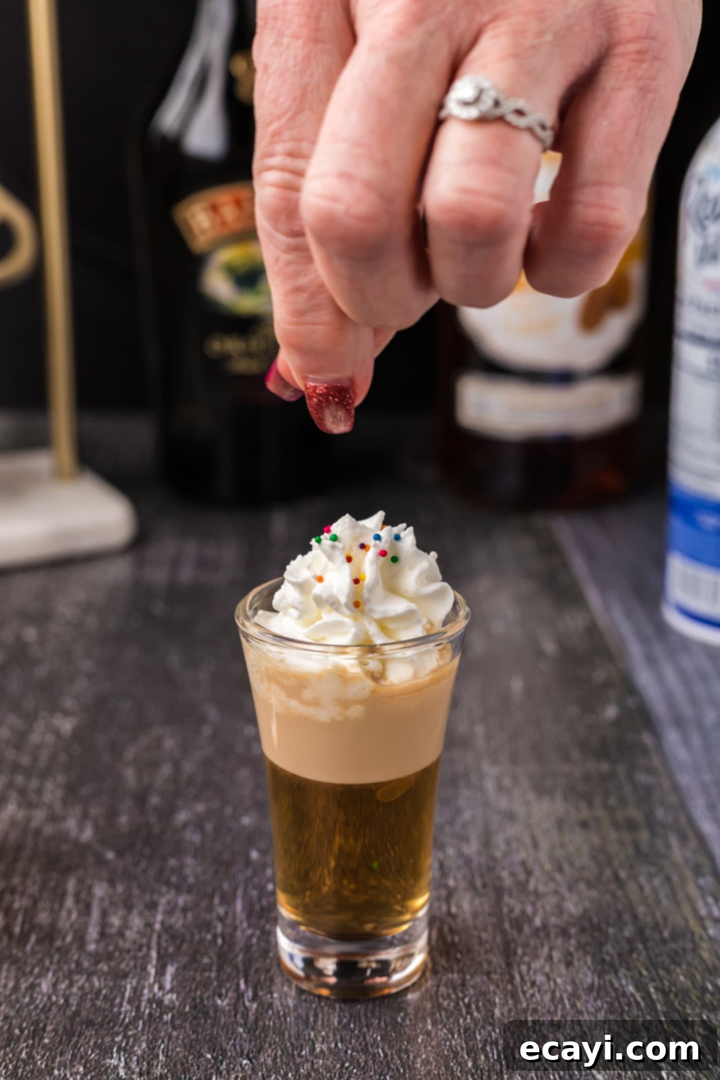 Buttery Nipple Bliss 10 Adding colorful sprinkles on top of whipped cream garnish for a Buttery Nipple Shot