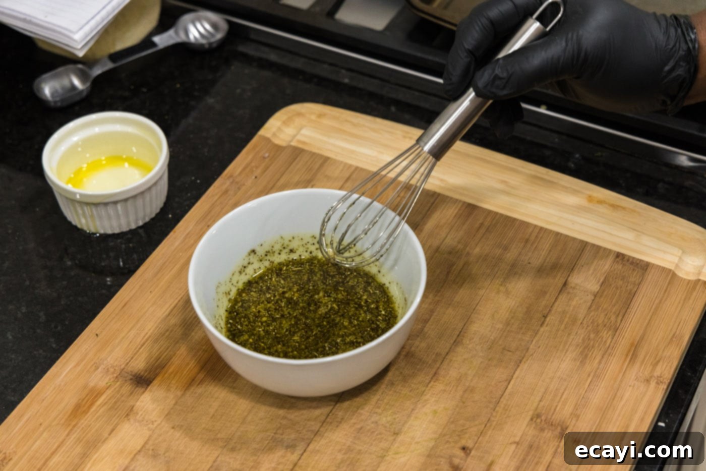 Smoky Zucchini Perfection 6 A hand whisking together olive oil with garlic and various seasonings in a glass bowl, creating a marinade for grilling.