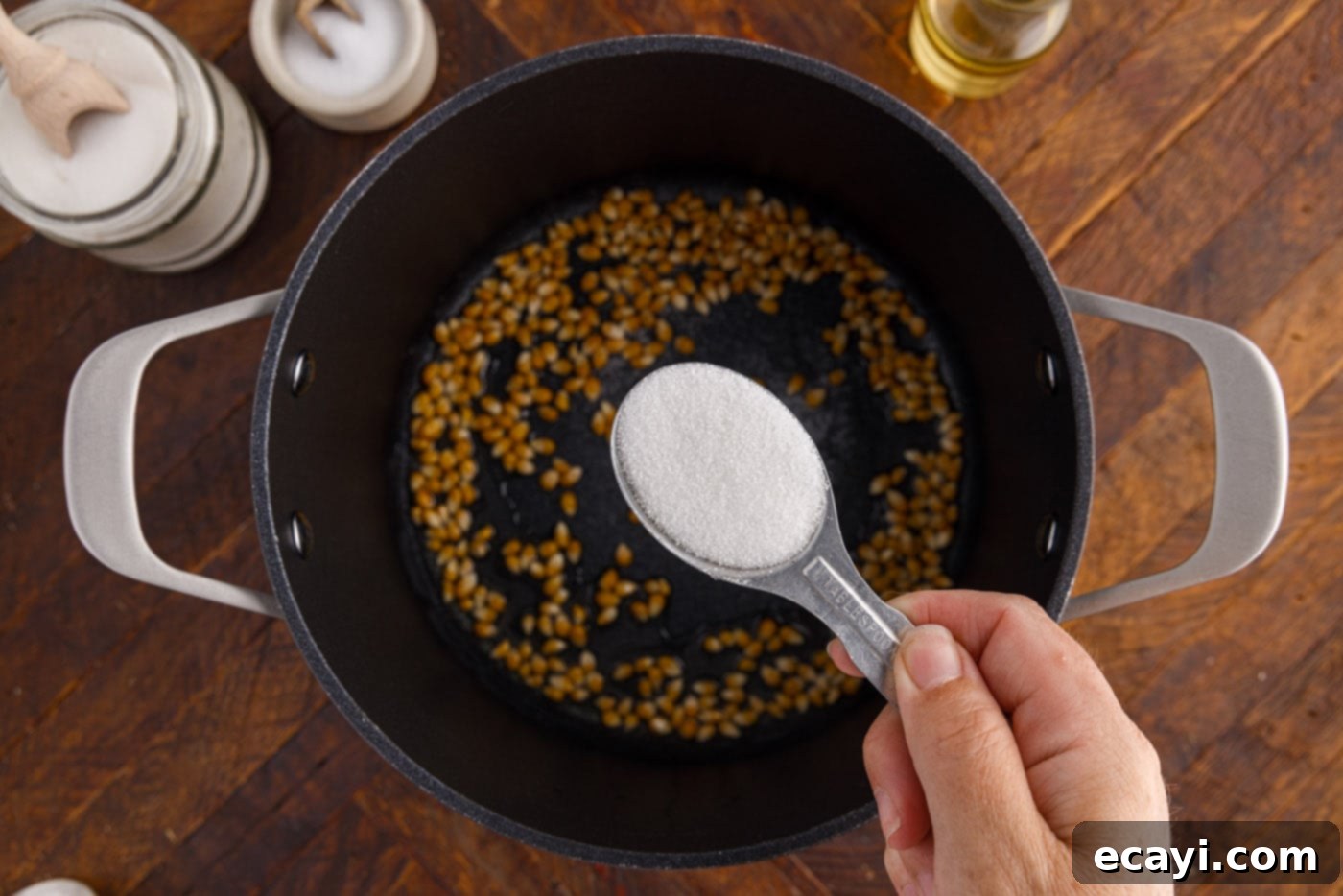Irresistible Sweet & Salty Crunch 7 Granulated sugar being sprinkled over corn kernels in the pot