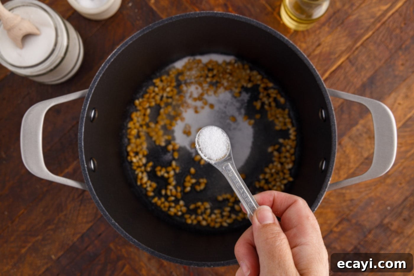 Irresistible Sweet & Salty Crunch 8 Sea salt being added to corn kernels and sugar in a cooking pot