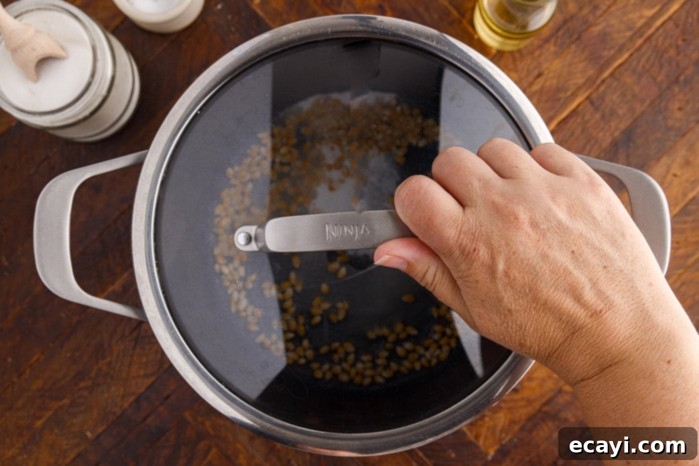 Irresistible Sweet & Salty Crunch 9 A lid being placed securely over a pot of popcorn kernels, sugar, and oil