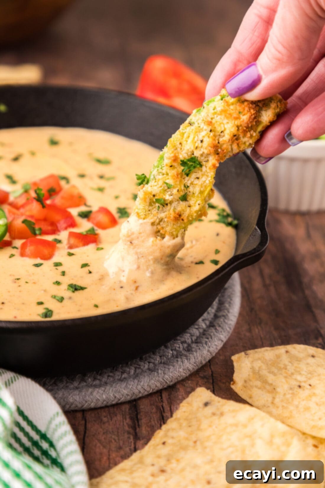 Creamy Queso 3 An air fryer avocado fry being dipped into a skillet of hot, creamy Queso Dip