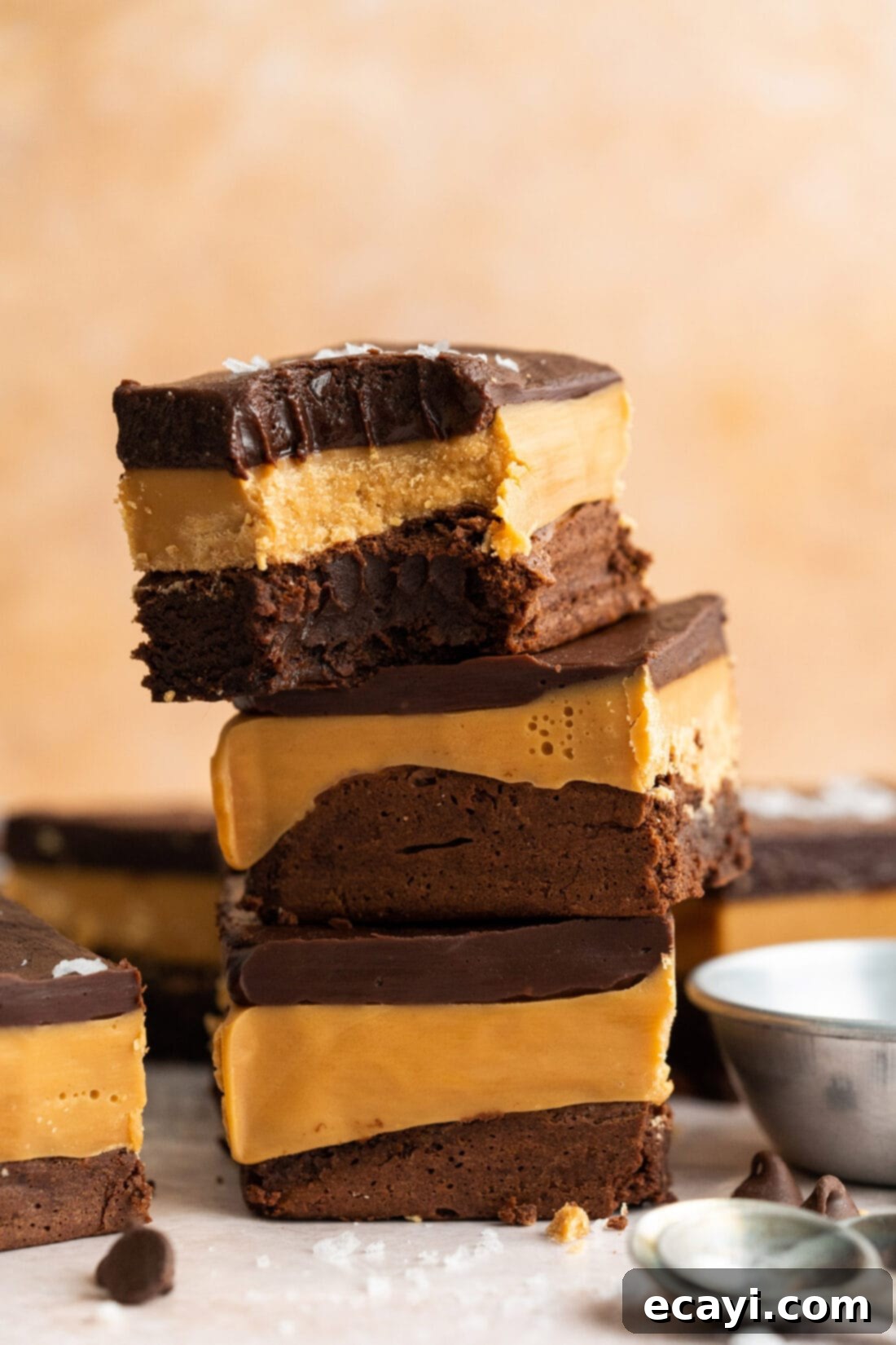 Decadent Millionaire Brownies 2 Stack of three Millionaire Brownies with a bite removed from the top one, showcasing the distinct layers of brownie, caramel, and chocolate ganache.