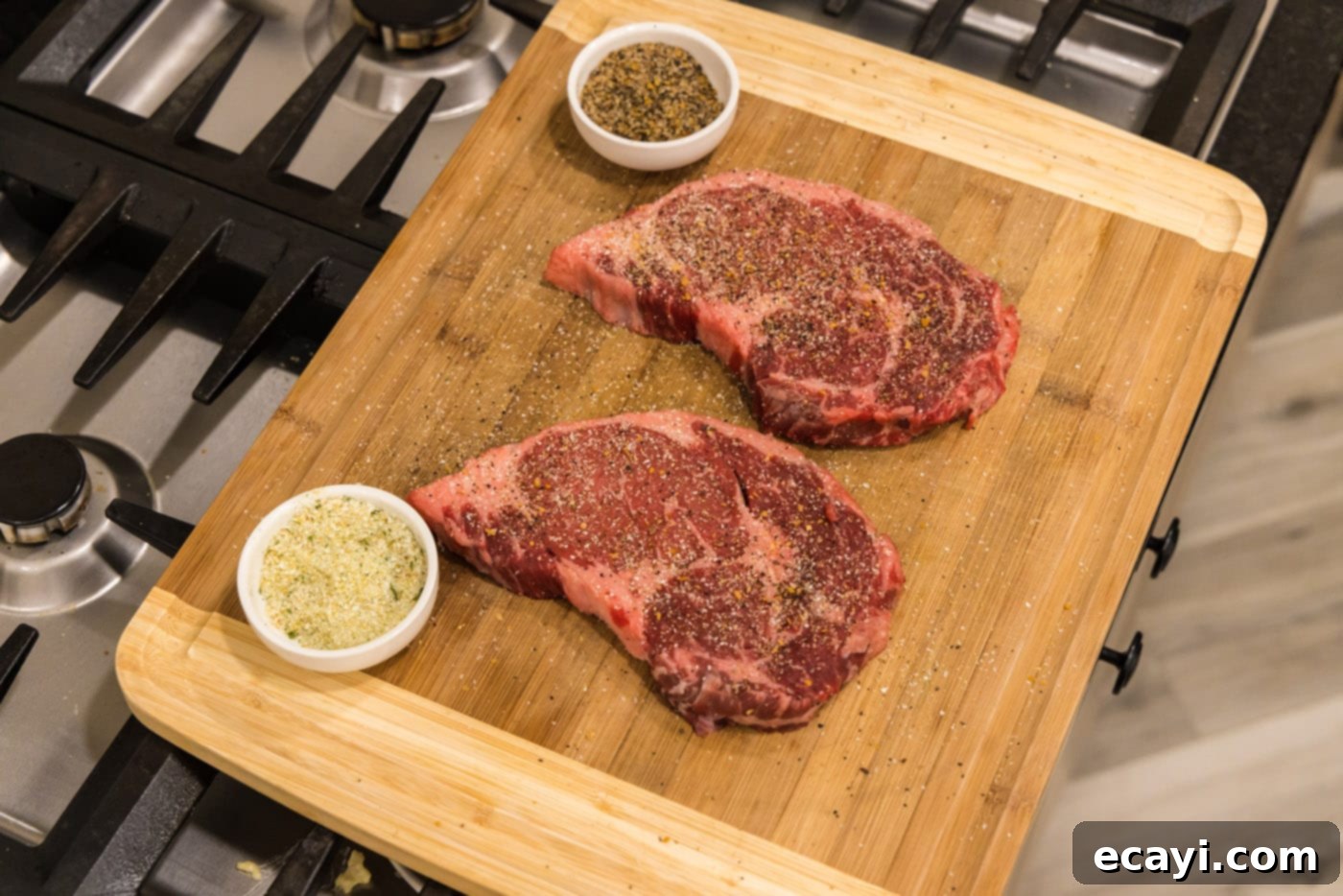 Restaurant-Quality Air Fryer Steak 5 Ribeye steaks on a cutting board, generously seasoned with garlic salt and steak seasoning.