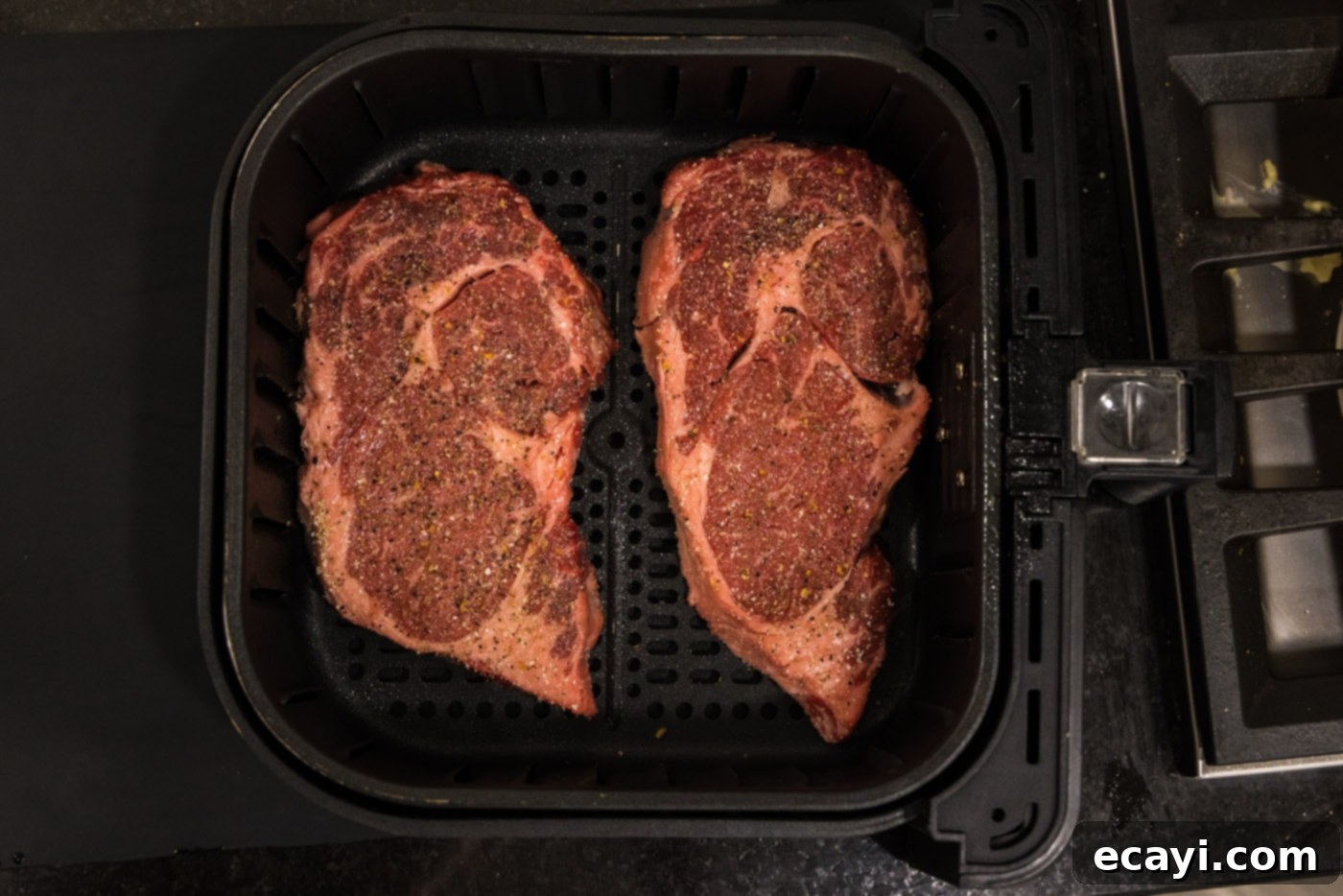 Restaurant-Quality Air Fryer Steak 6 Ribeye steaks cooking in the air fryer basket.