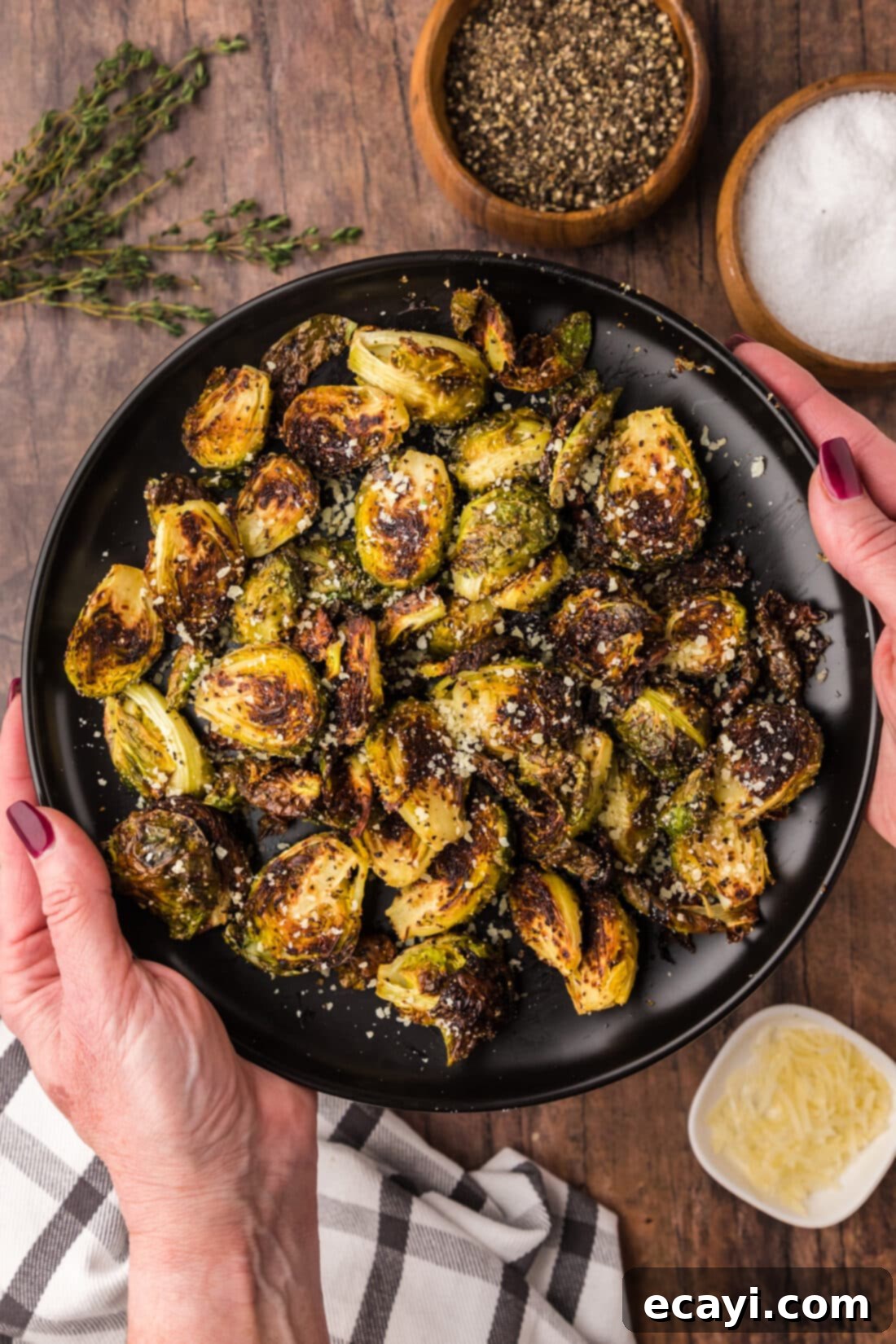 Crispy Roasted Brussels Sprouts 5 Hands holding a plate of Roasted Brussel Sprouts topped with parmesan, ready to be served.