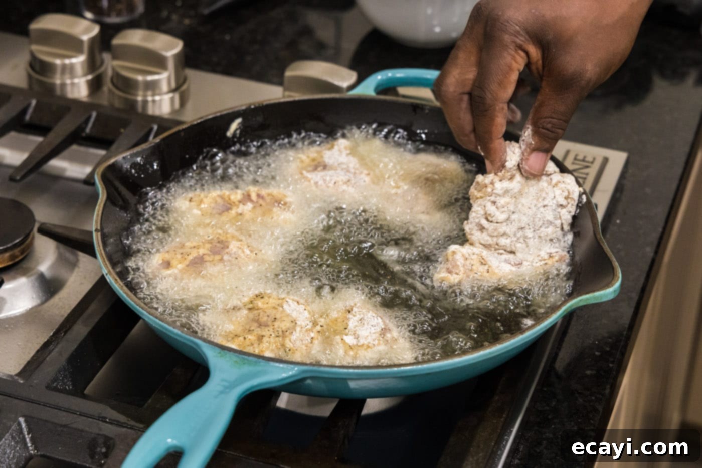 Southern Comfort Bliss 12 Dredged chicken thighs being carefully placed into hot frying oil