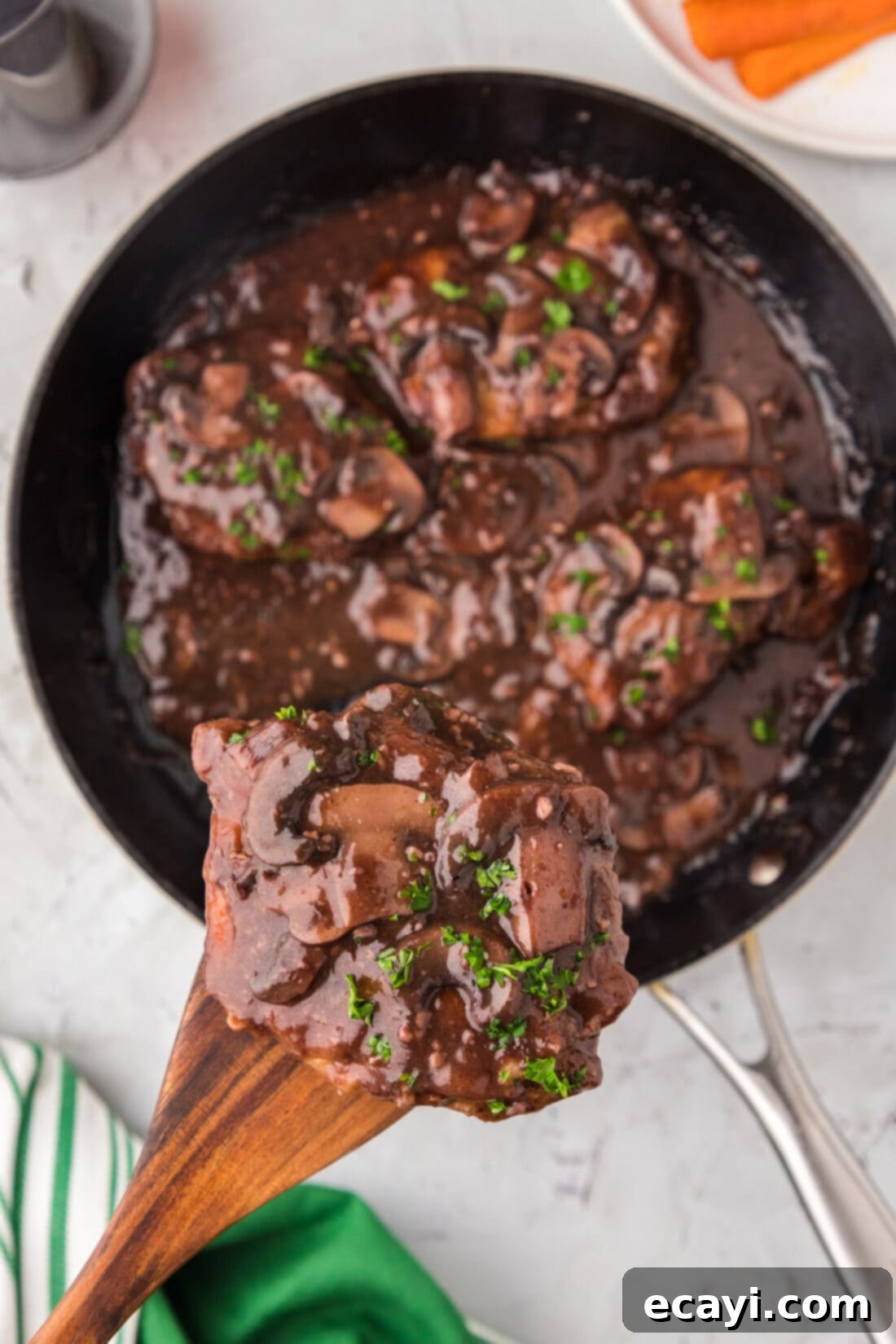Classic Veal Marsala 15 A wooden spatula lifting a piece of tender Veal Marsala from a skillet, showcasing the rich sauce.