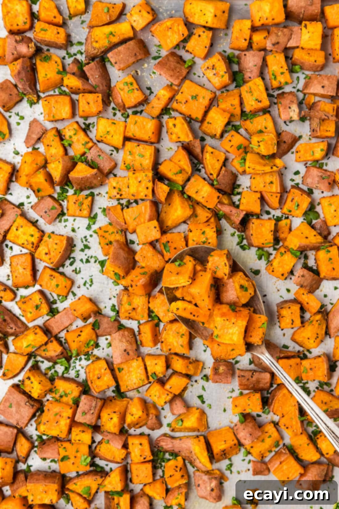 The Ultimate Roasted Sweet Potatoes 2 Sheet pan of Roasted Sweet Potatoes with a spoon on the sheet pan