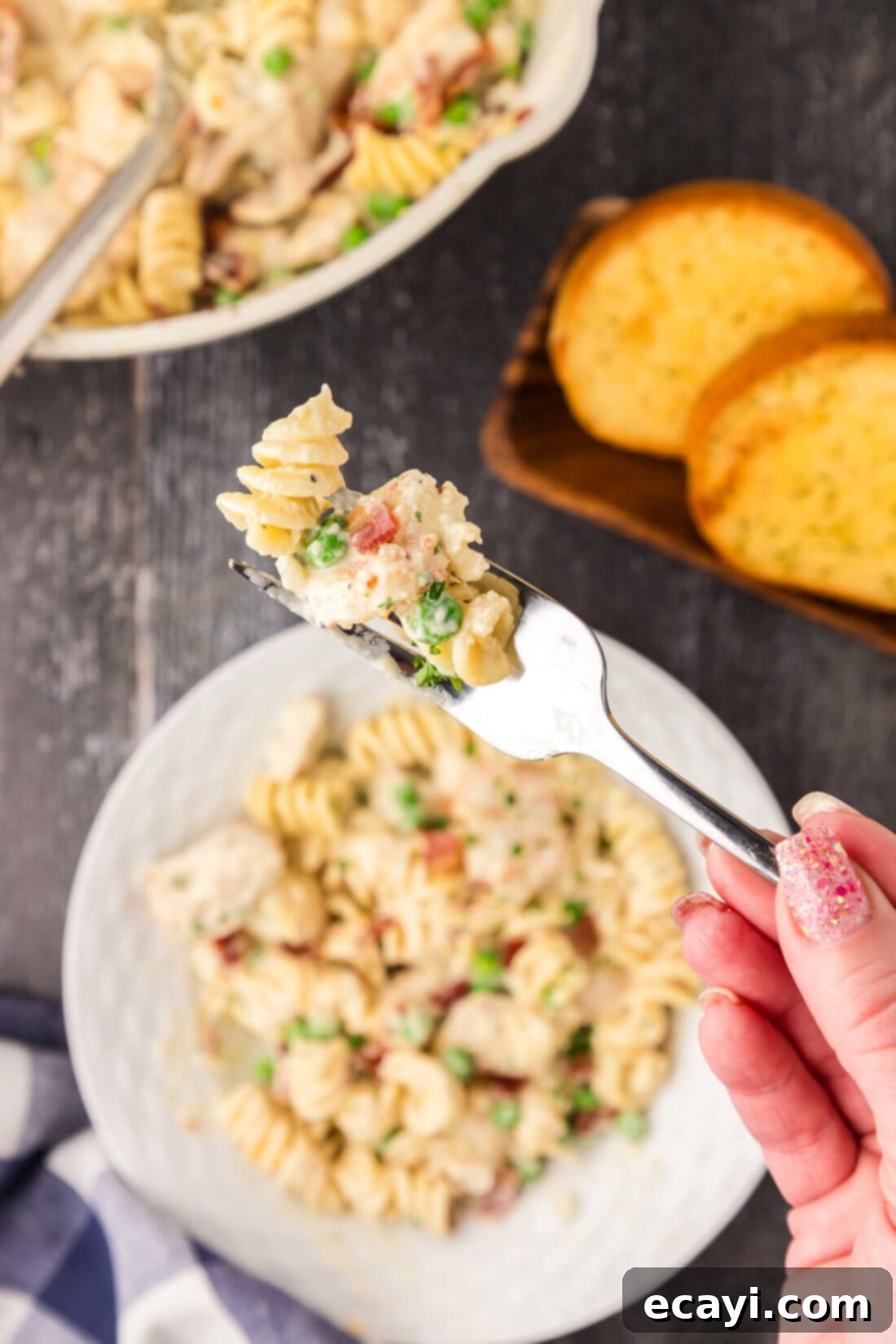Surf and Turf Carbonara 17 A fork holding a portion of Chicken and Shrimp Carbonara, lifted above a full bowl, highlighting the perfectly coated pasta and ingredients.