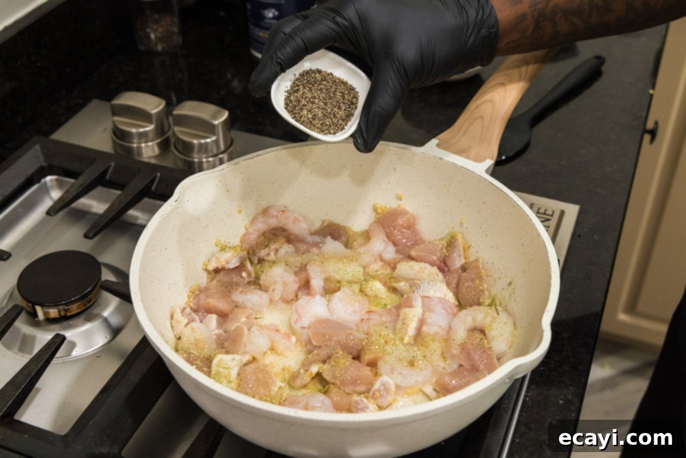 Surf and Turf Carbonara 6 adding seasoning to skillet of shrimp, chicken, and garlic.
