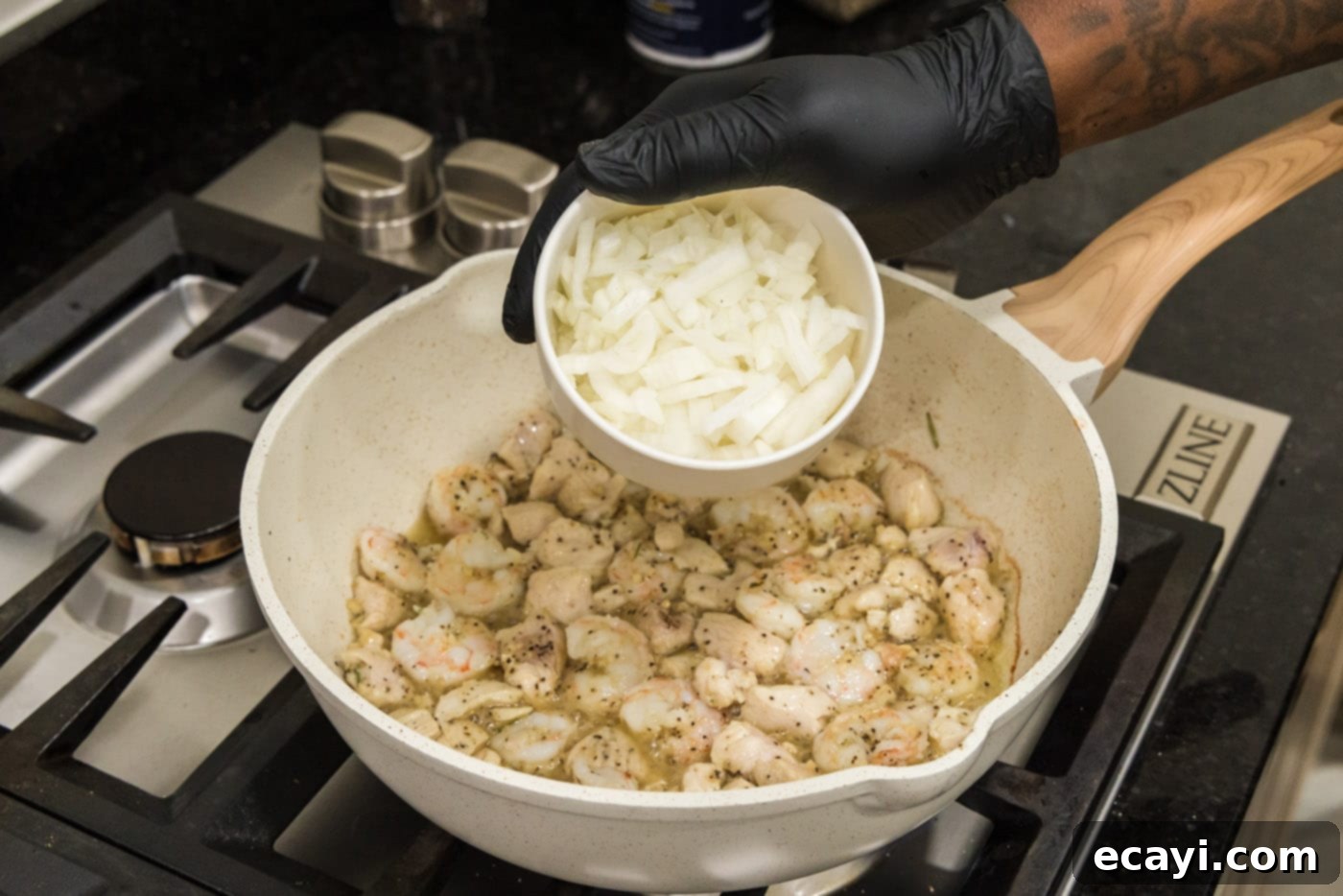 Surf and Turf Carbonara 7 Hand adding chopped onion to skillet with chicken and shrimp mixture