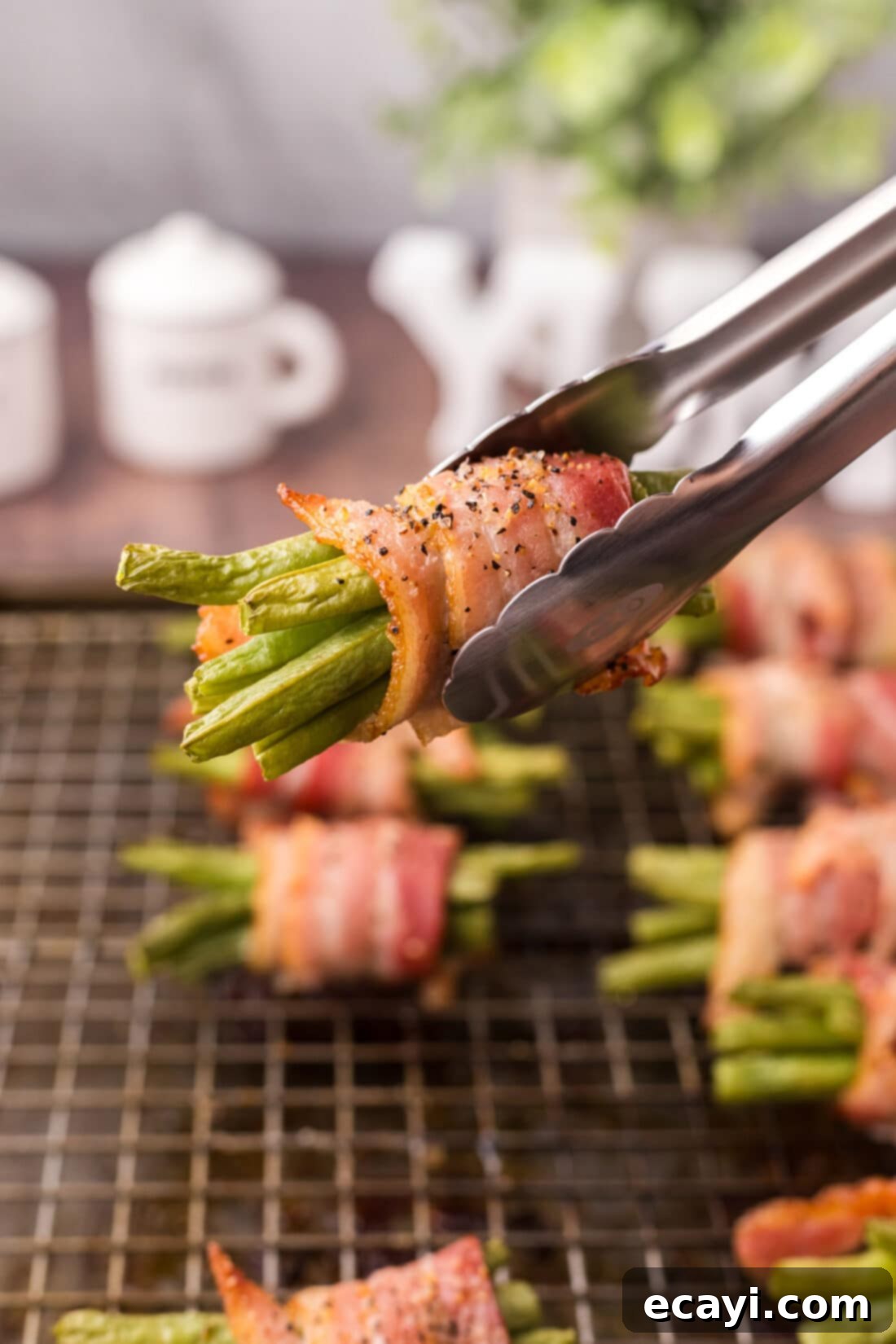 Bacon Green Bean Bundles 11 Tongs holding up a perfectly baked Bacon Wrapped Green Bean bundle, highlighting its crispiness