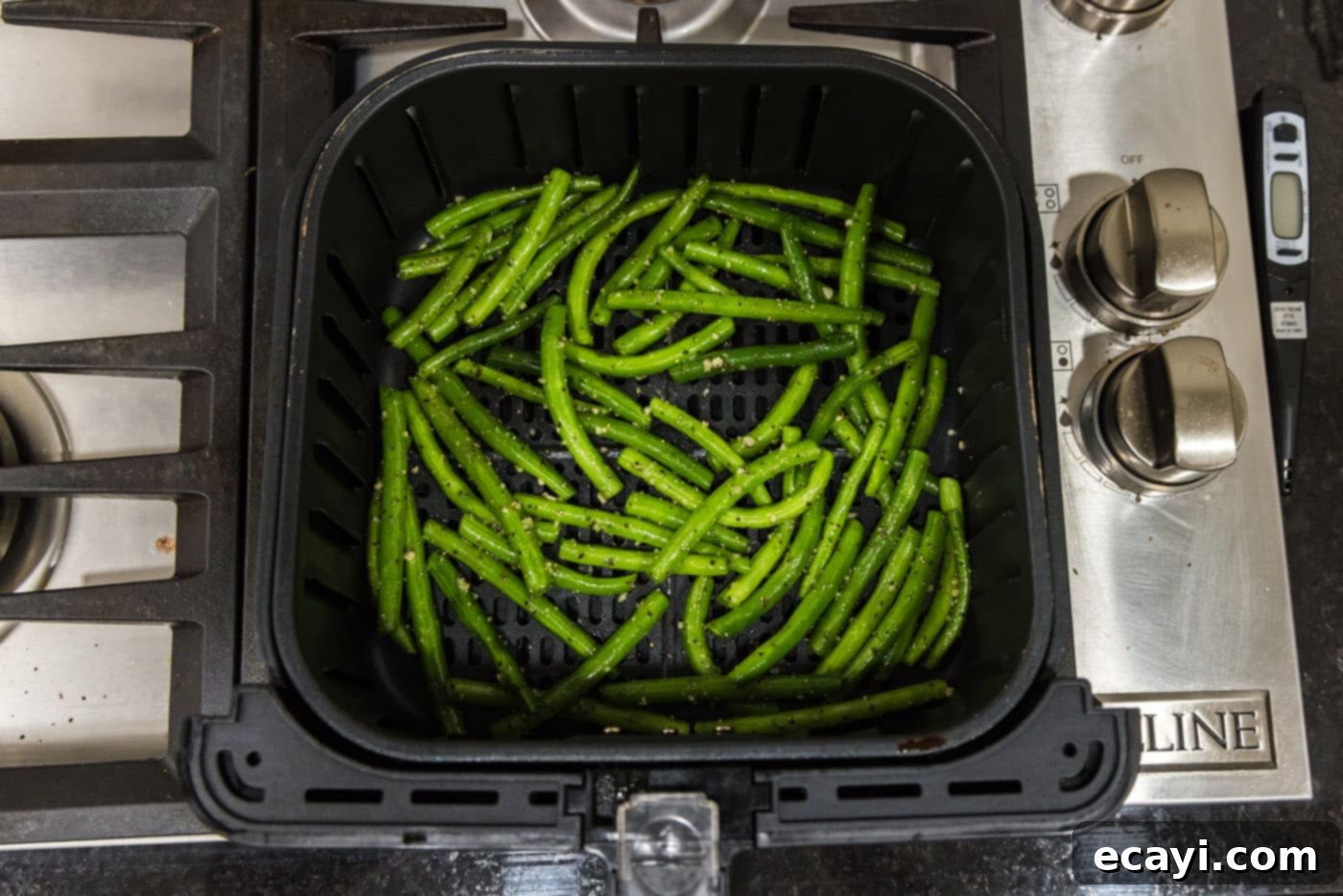 Crispy Air Fryer Green Beans 7 Fresh green beans with seasoning and garlic neatly arranged in a single layer in an air fryer basket, ready to cook.