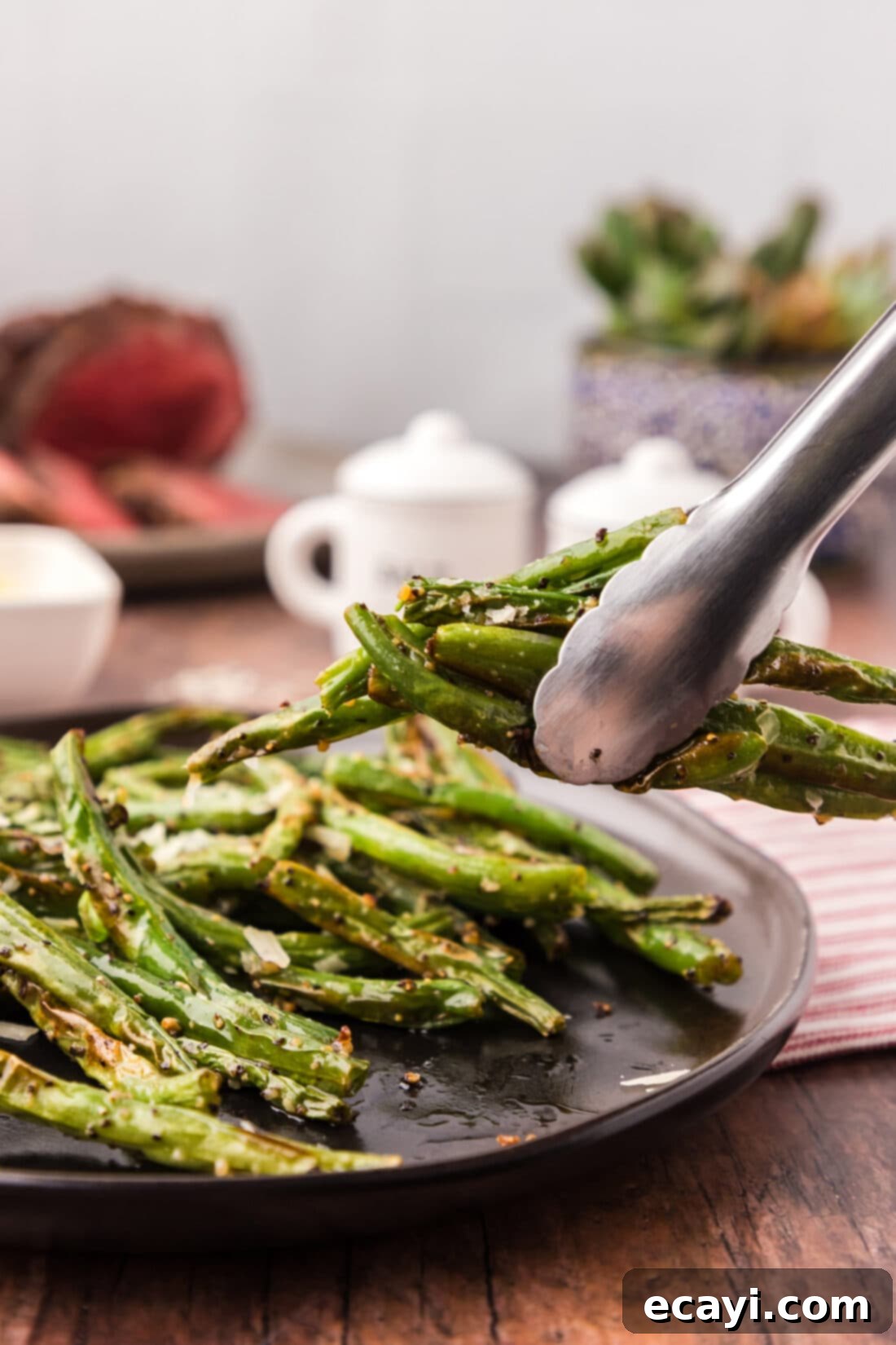 Crispy Air Fryer Green Beans 9 Tongs holding a portion of Air Fryer Green Beans over a serving plate, highlighting their perfect readiness.