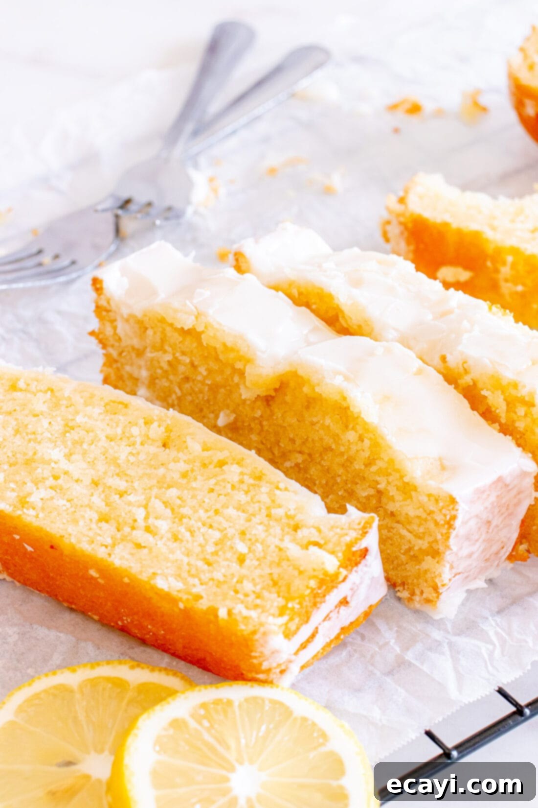 Zesty Lemon Loaf 15 Several slices of glazed Lemon Pound Cake arranged artfully on parchment paper, ready to be served.