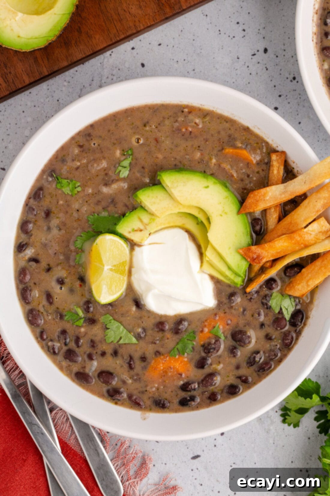 Savory Black Bean Delight 2 A beautifully presented bowl of creamy black bean soup, garnished with a dollop of sour cream, slices of fresh avocado, and a sprinkle of vibrant cilantro, invitingly placed on a rustic table setting.