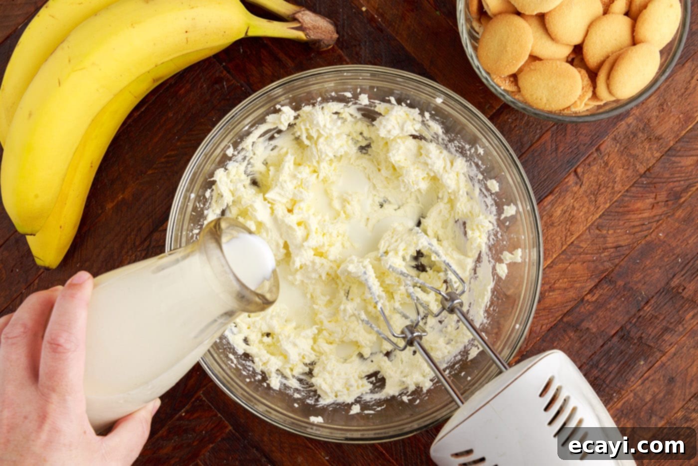 Decadent Banana Layers 5 adding whole milk to whipped cream cheese in a bowl with a mixer