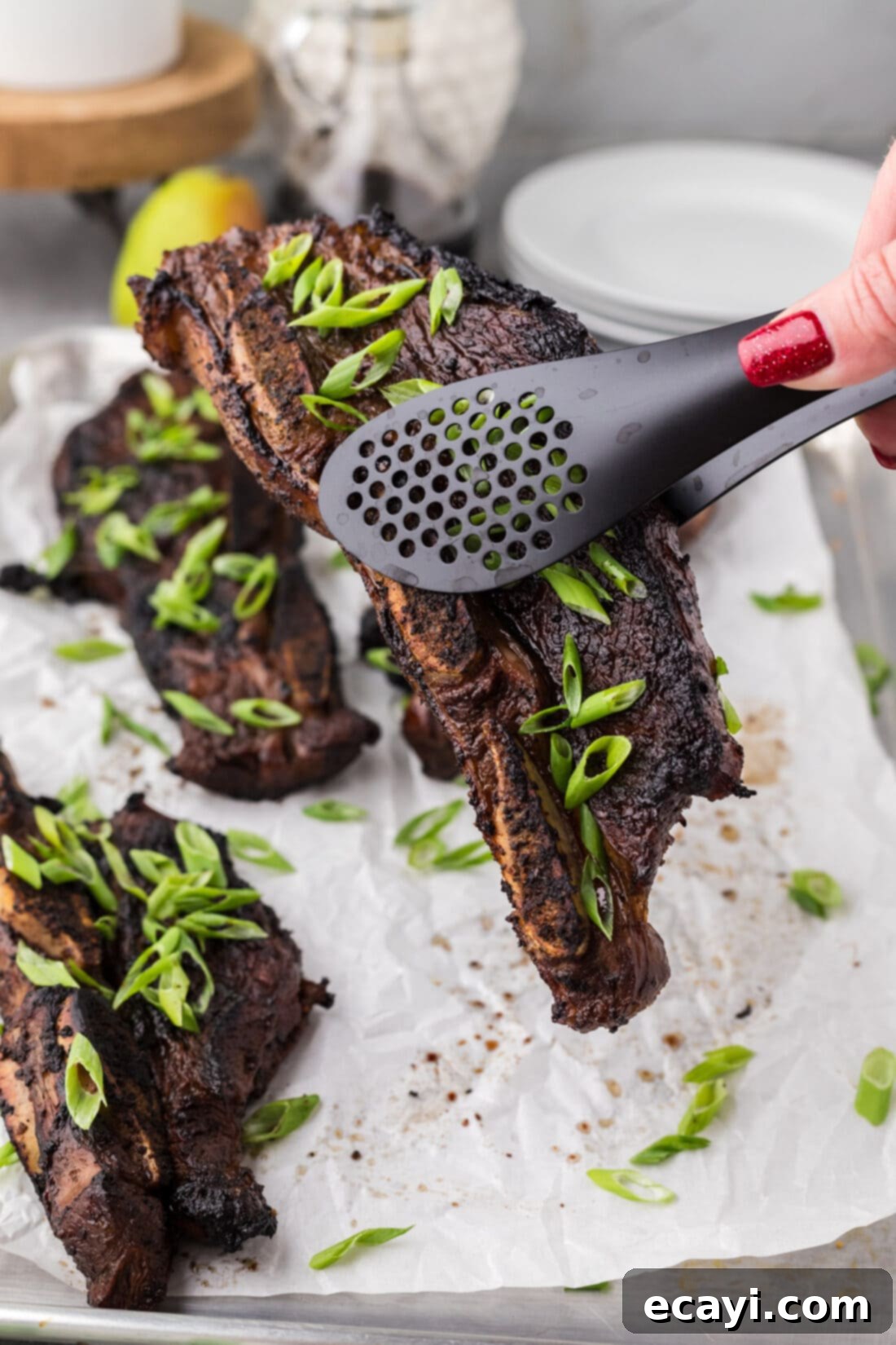 Fall-Off-The-Bone Korean Short Ribs 2 Tongs holding up a perfectly grilled Korean Short Rib, showing off its caramelized exterior and juicy interior.