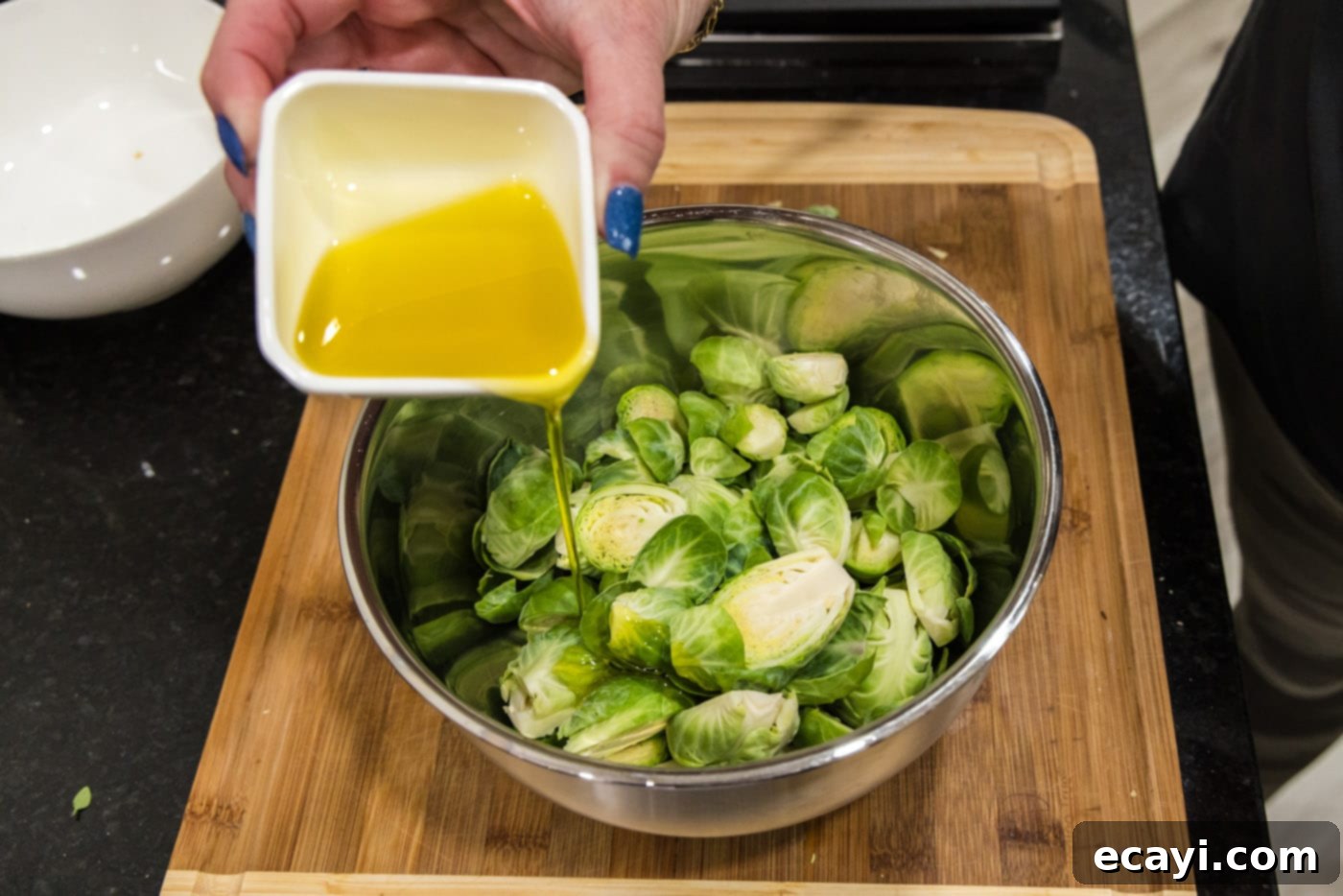 Roasted Brussels Sprouts with Crispy Bacon and Glazed Pecans 6 Adding olive oil to a bowl of halved Brussels sprouts, preparing to toss.