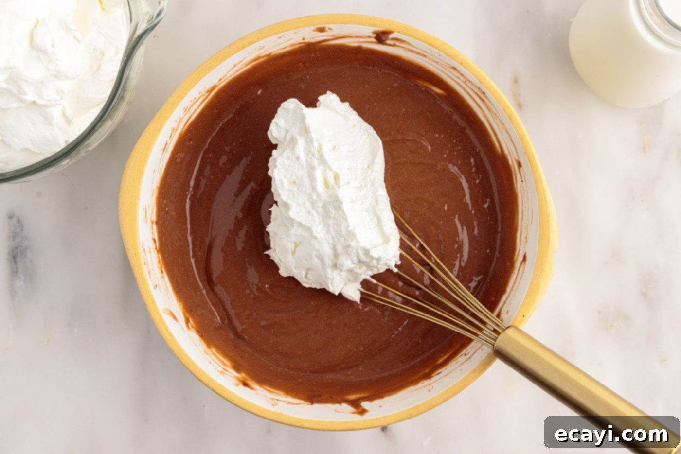 Decadent Brownie Trifle 8 Adding a scoop of fluffy whipped cream to the chocolate pudding mixture in a bowl.