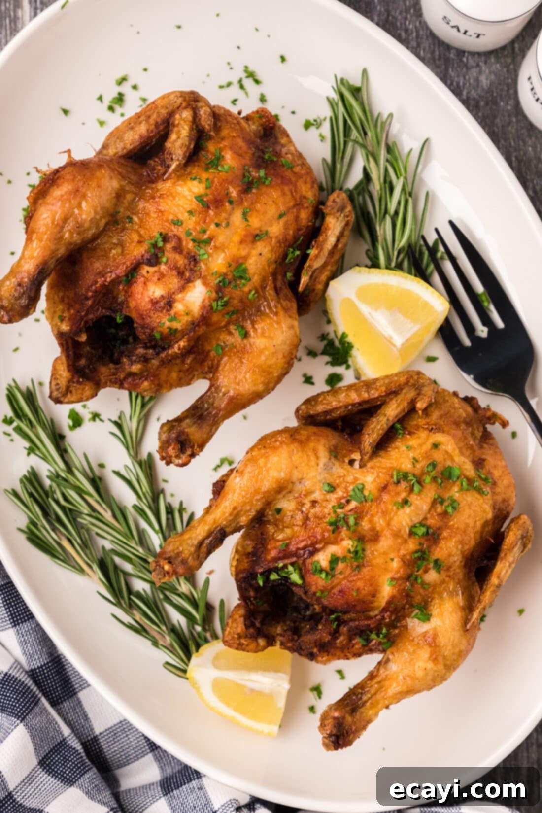 Crispy Golden Cornish Hens 2 Deep Fried Cornish Hens on a platter with lemons and herbs, showcasing crispy golden-brown skin
