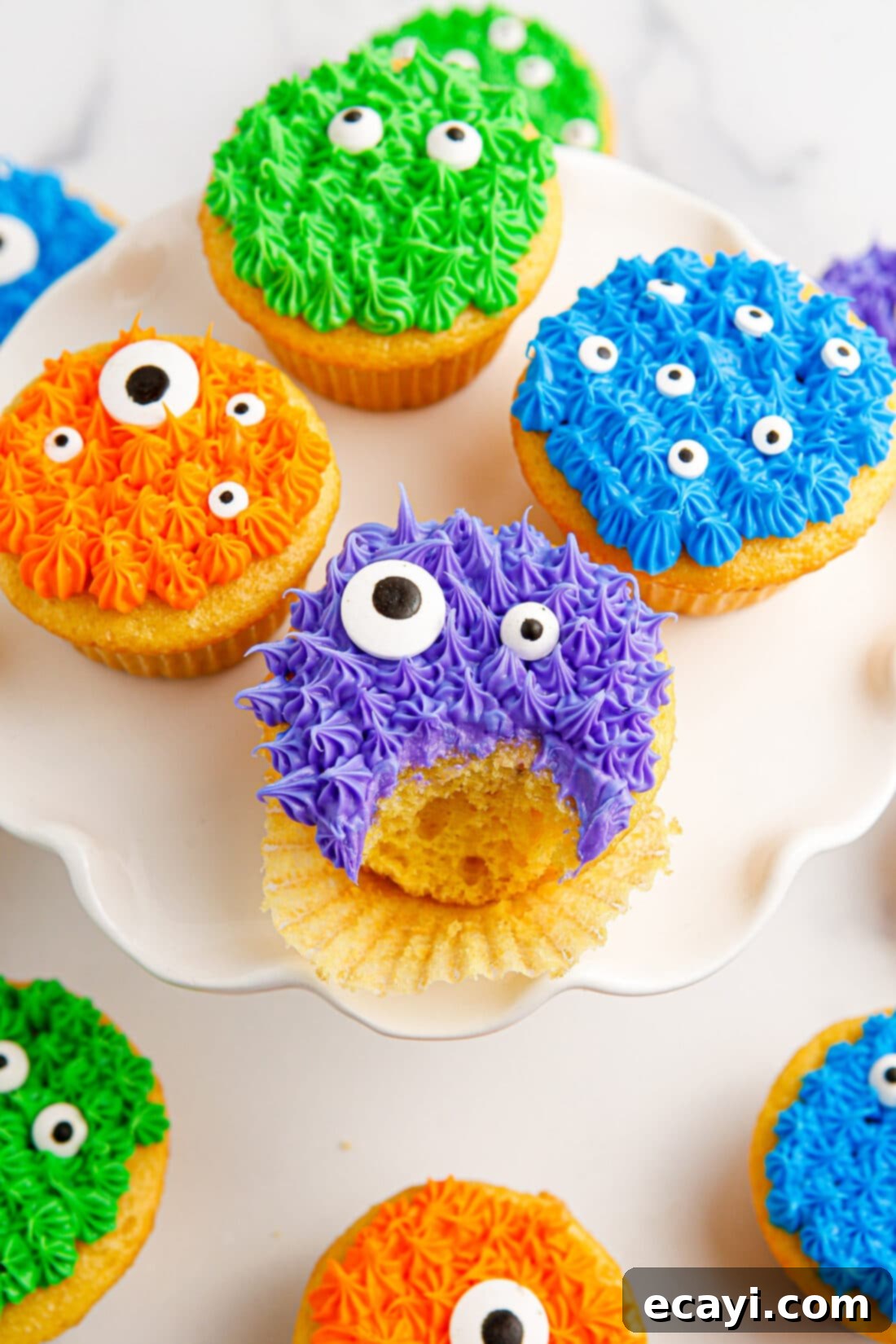 Ghoul-icious Cupcakes 2 Monster Cupcakes on a cake stand with a bite taken out of one, showcasing vibrant frosting and candy eyes