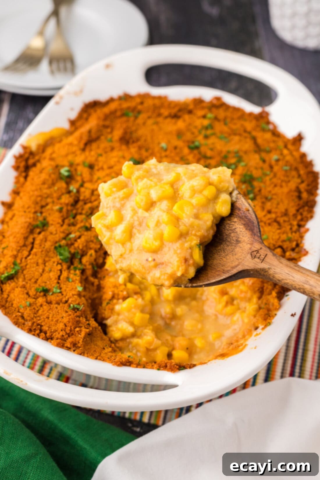 Creamy Baked Corn 2 Spoonful of golden, bubbly Scalloped Corn Casserole being lifted out of the baking dish, showing creamy corn mixture and crunchy cracker topping
