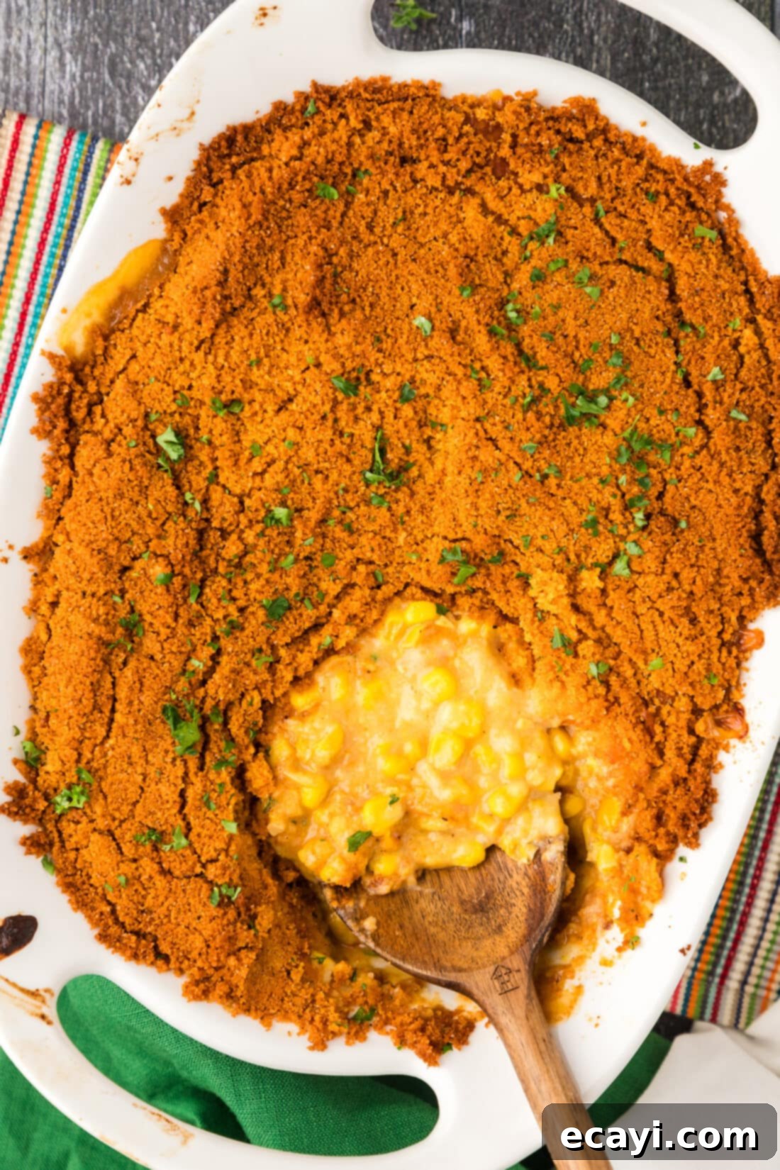 Creamy Baked Corn 15 Large pan of freshly baked Scalloped Corn Casserole with a serving spoon resting in it, showing the cheesy, creamy interior and golden, crunchy topping