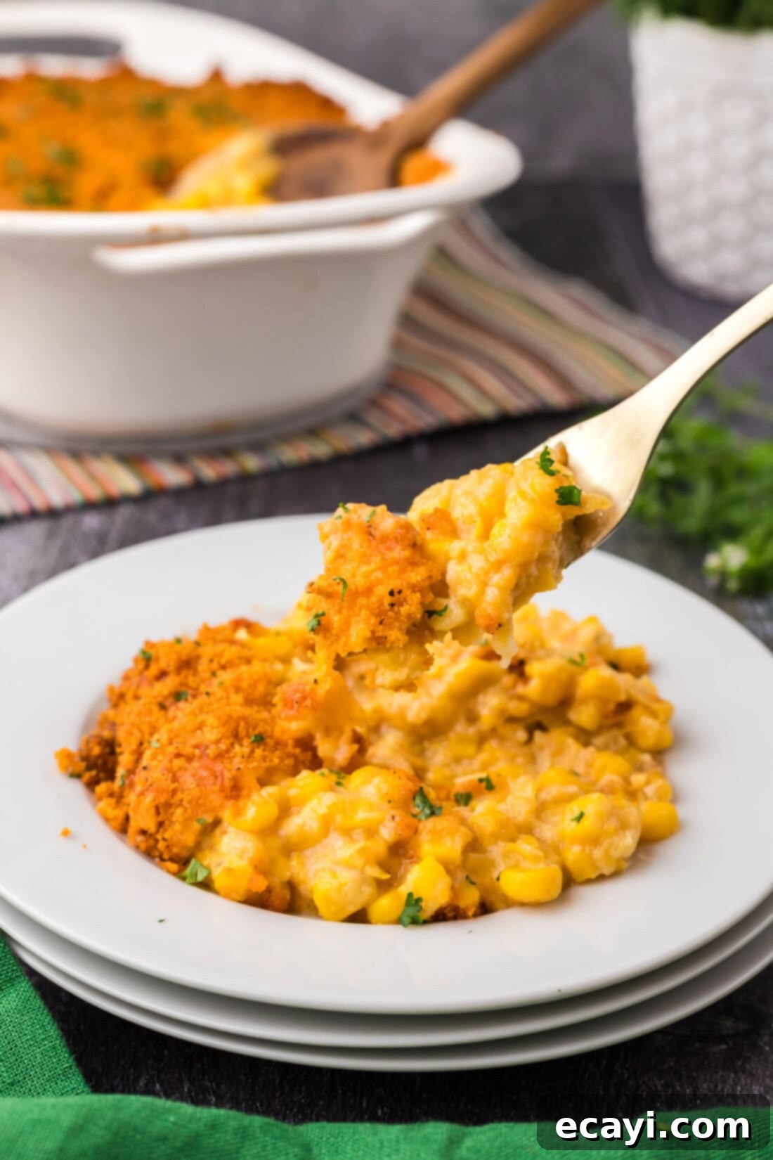 Creamy Baked Corn 3 Forkful of creamy Scalloped Corn with golden cracker topping lifted from a white plate, ready to be eaten