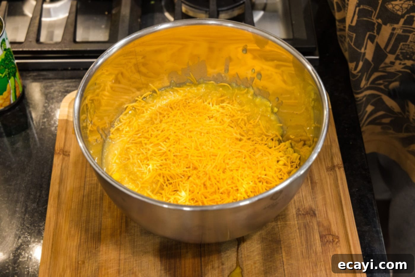 Creamy Baked Corn 9 Shredded cheddar cheese being added to the corn mixture in a large mixing bowl