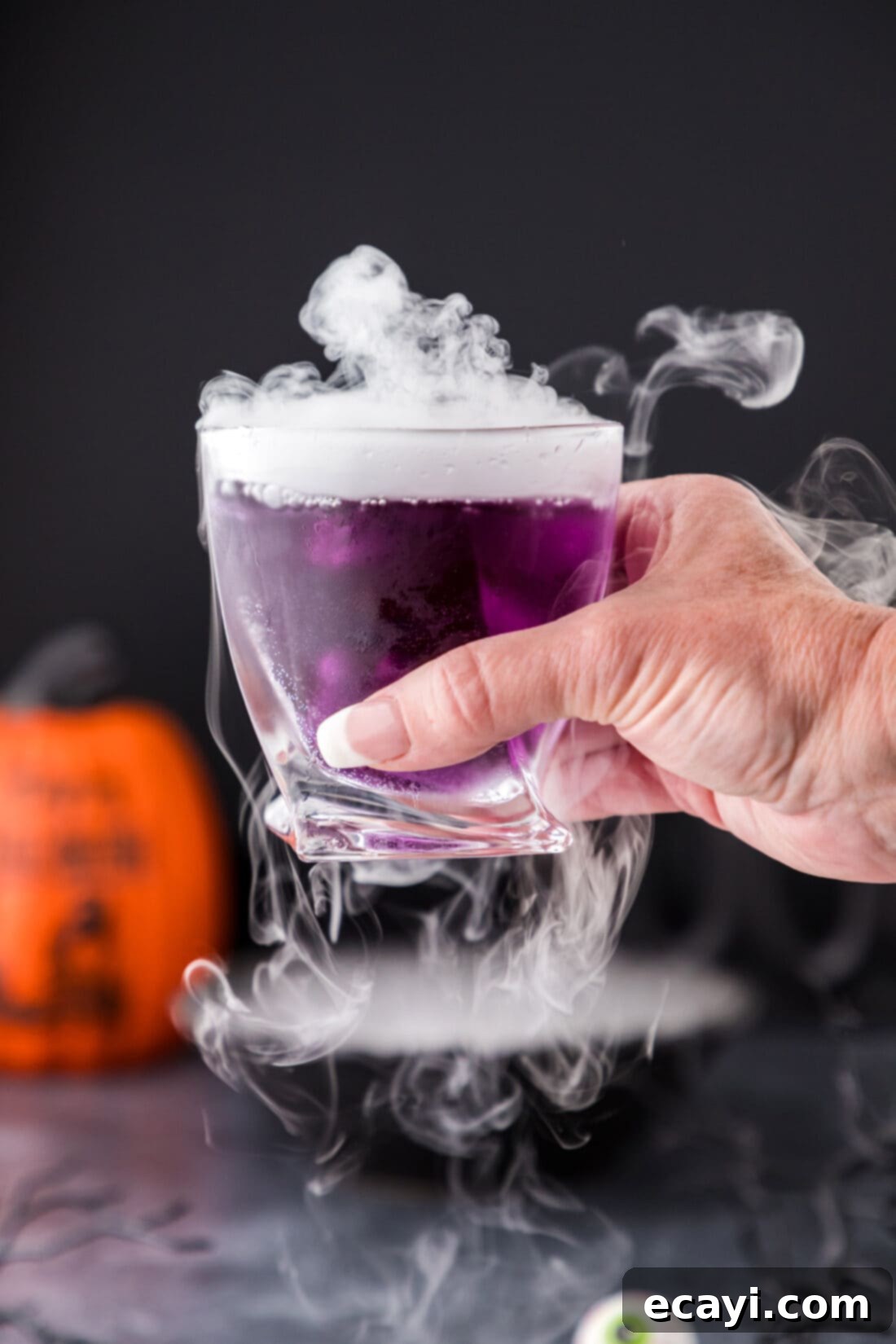 Amethyst Abyss Elixir 3 Hand holding up a Purple People Eater Cocktail in a beaker glass