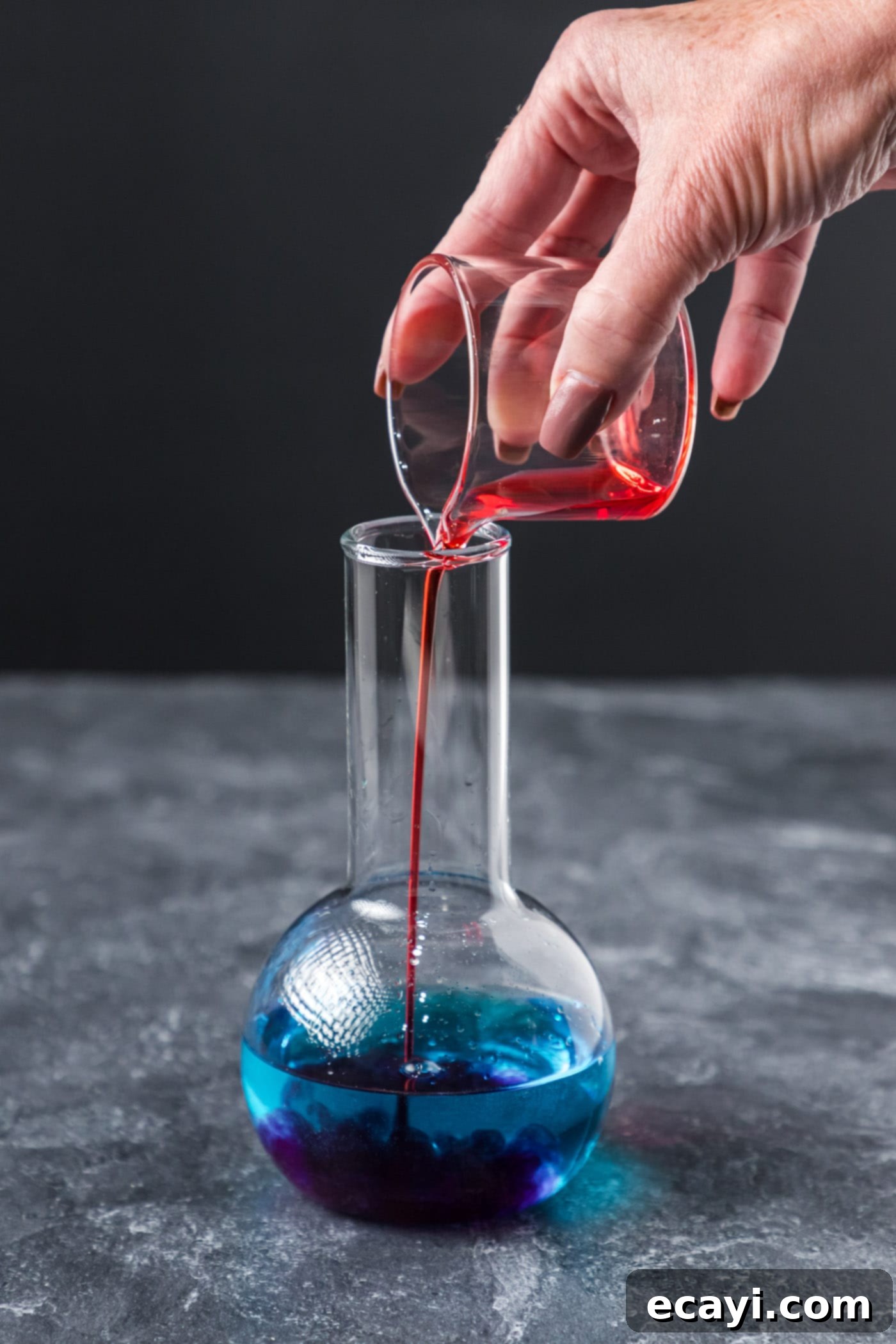Amethyst Abyss Elixir 7 pouring grenadine into cocktail glass with blue curacao and coconut rum
