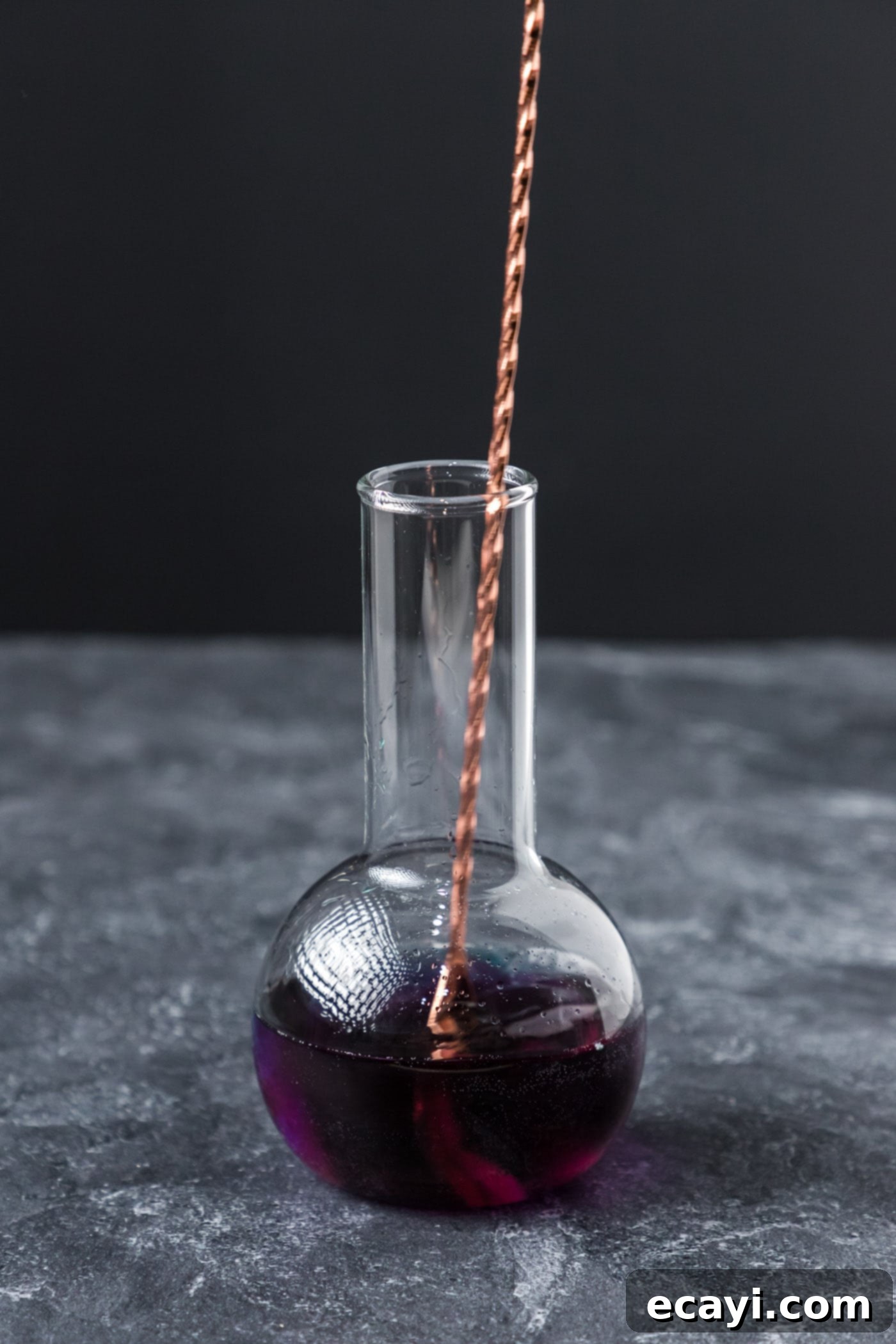 Amethyst Abyss Elixir 9 stirring purple people eater in a beaker cocktail glass