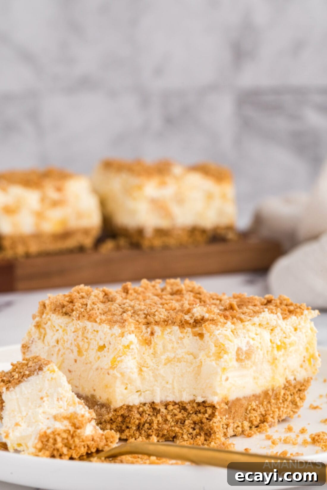 Pineapple dream is one of those perfect potluck desserts. Cream cheese, pineapple, whipped cream and graham crackers, yum! A delectable slice of Pineapple Dream Dessert with a single bite removed, revealing its creamy layers and crunchy graham cracker crust, perfect for any potluck or family gathering.