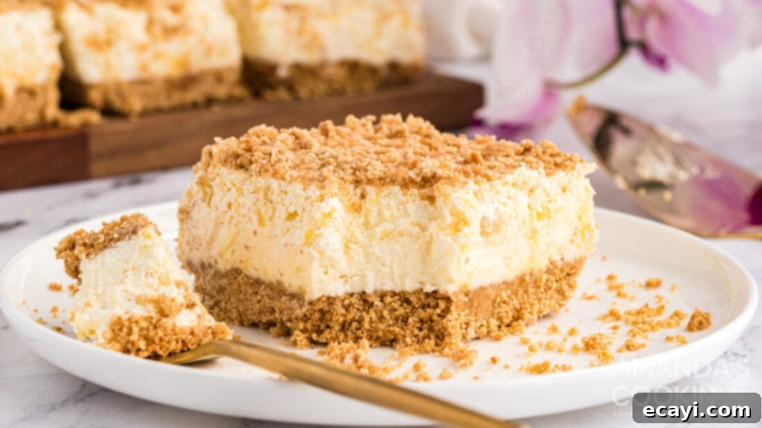 Pineapple dream is one of those perfect potluck desserts. Cream cheese, pineapple, whipped cream and graham crackers, yum! A close-up shot of a square piece of Pineapple Dream Dessert with a bite taken out, showcasing the distinct layers and inviting texture.