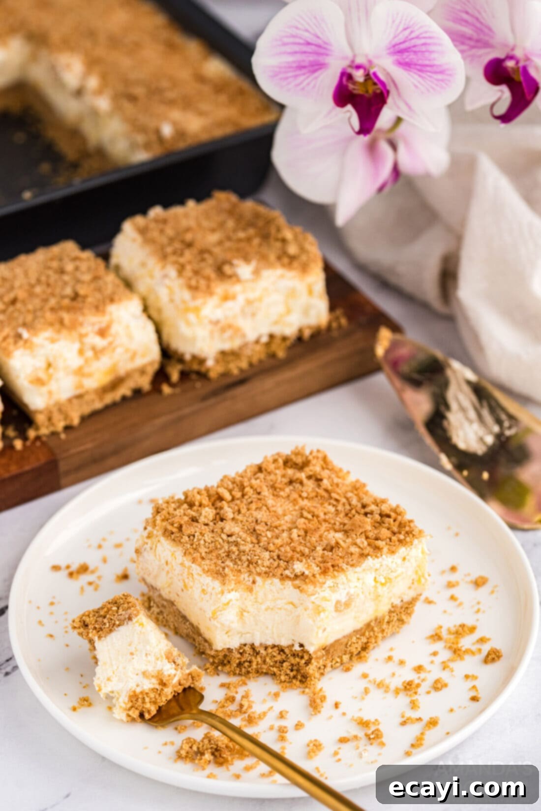 Pineapple dream is one of those perfect potluck desserts. Cream cheese, pineapple, whipped cream and graham crackers, yum! A perfectly cut square of Pineapple Dream Dessert presented on a white plate, ready to be enjoyed.
