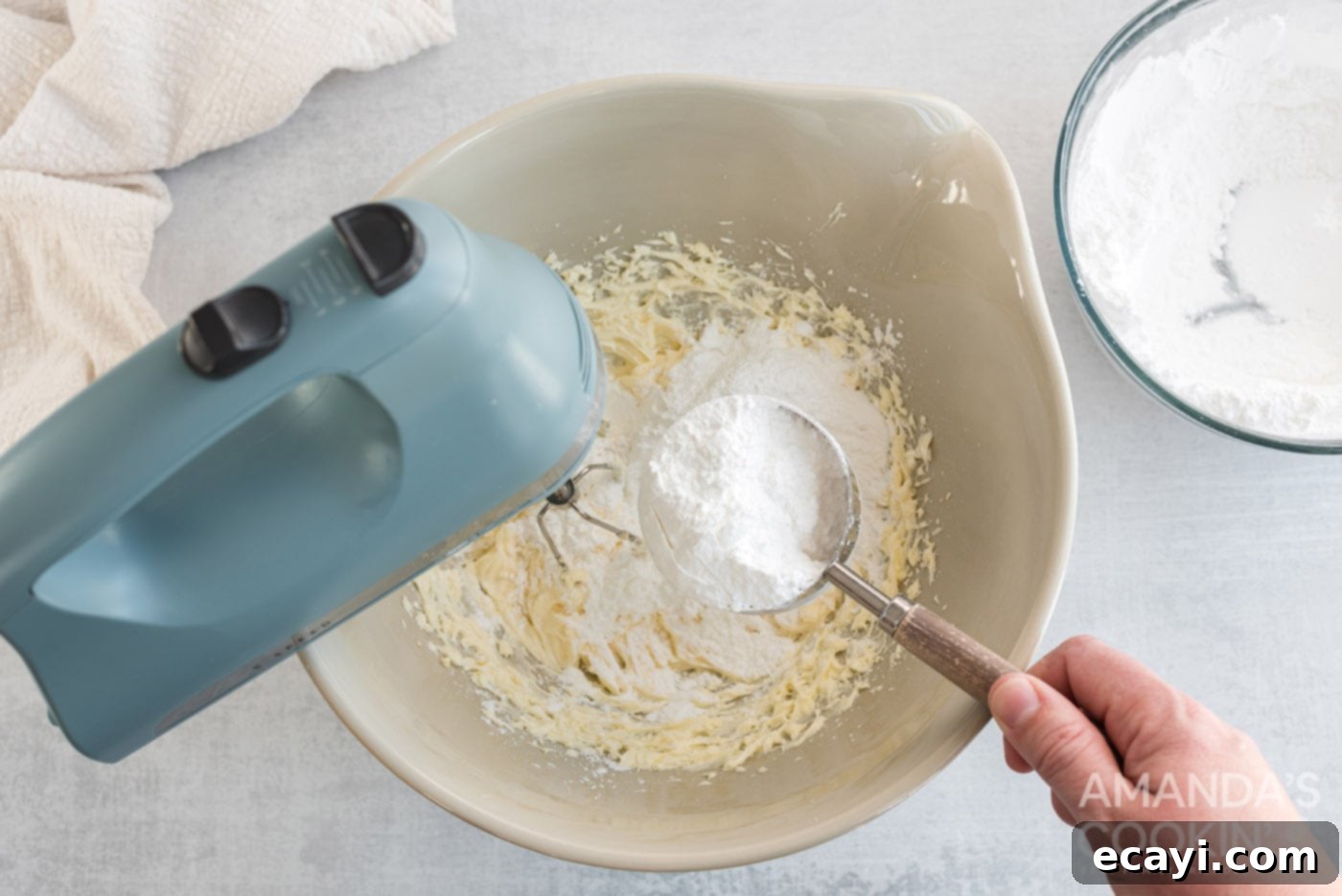 Pineapple Cloud Delight 6 Powdered sugar being slowly added to a mixing bowl containing beaten cream cheese and butter for the dessert filling.