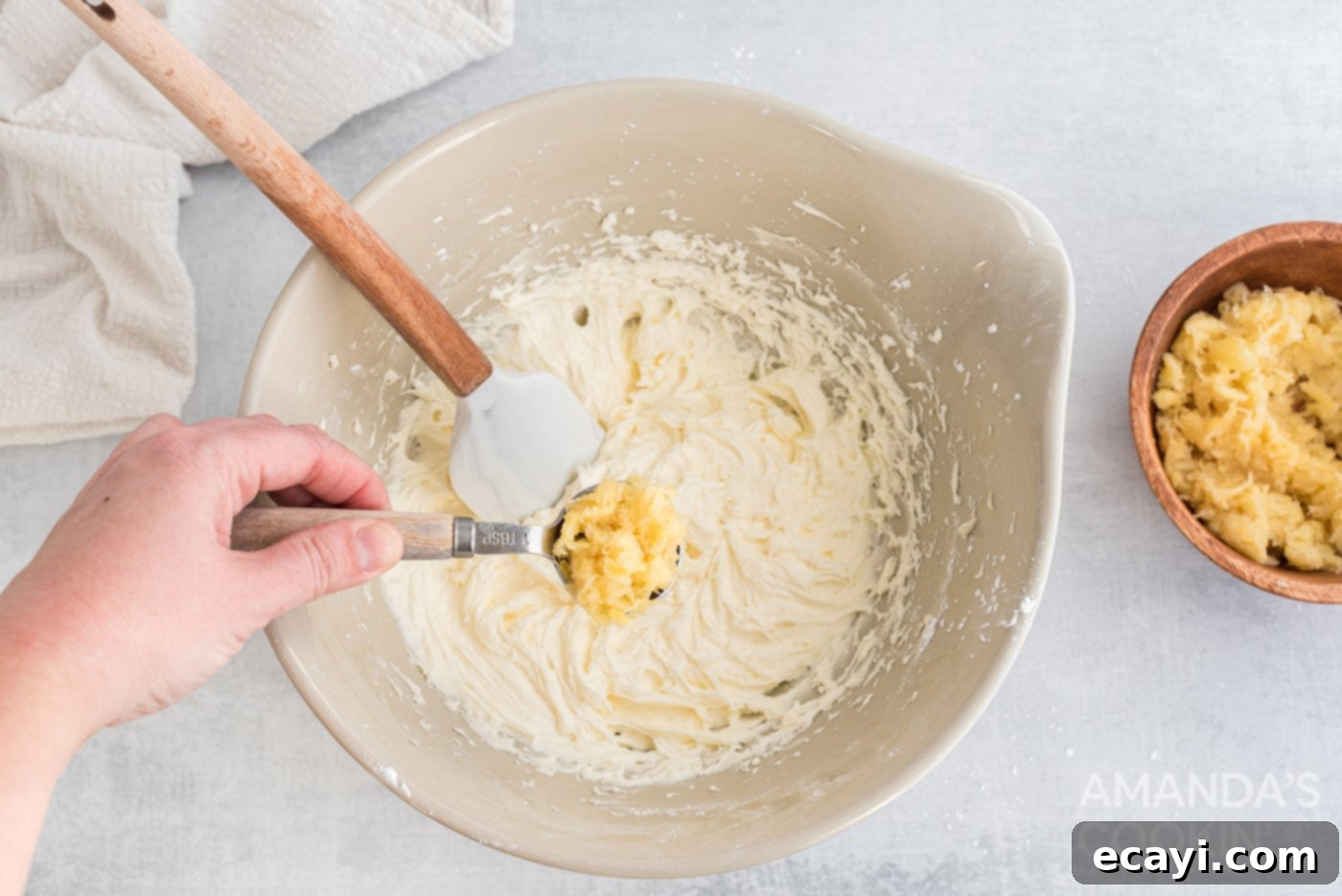 Pineapple Cloud Delight 7 A tablespoon of drained crushed pineapple being stirred into the creamy cheese mixture using a rubber spatula.